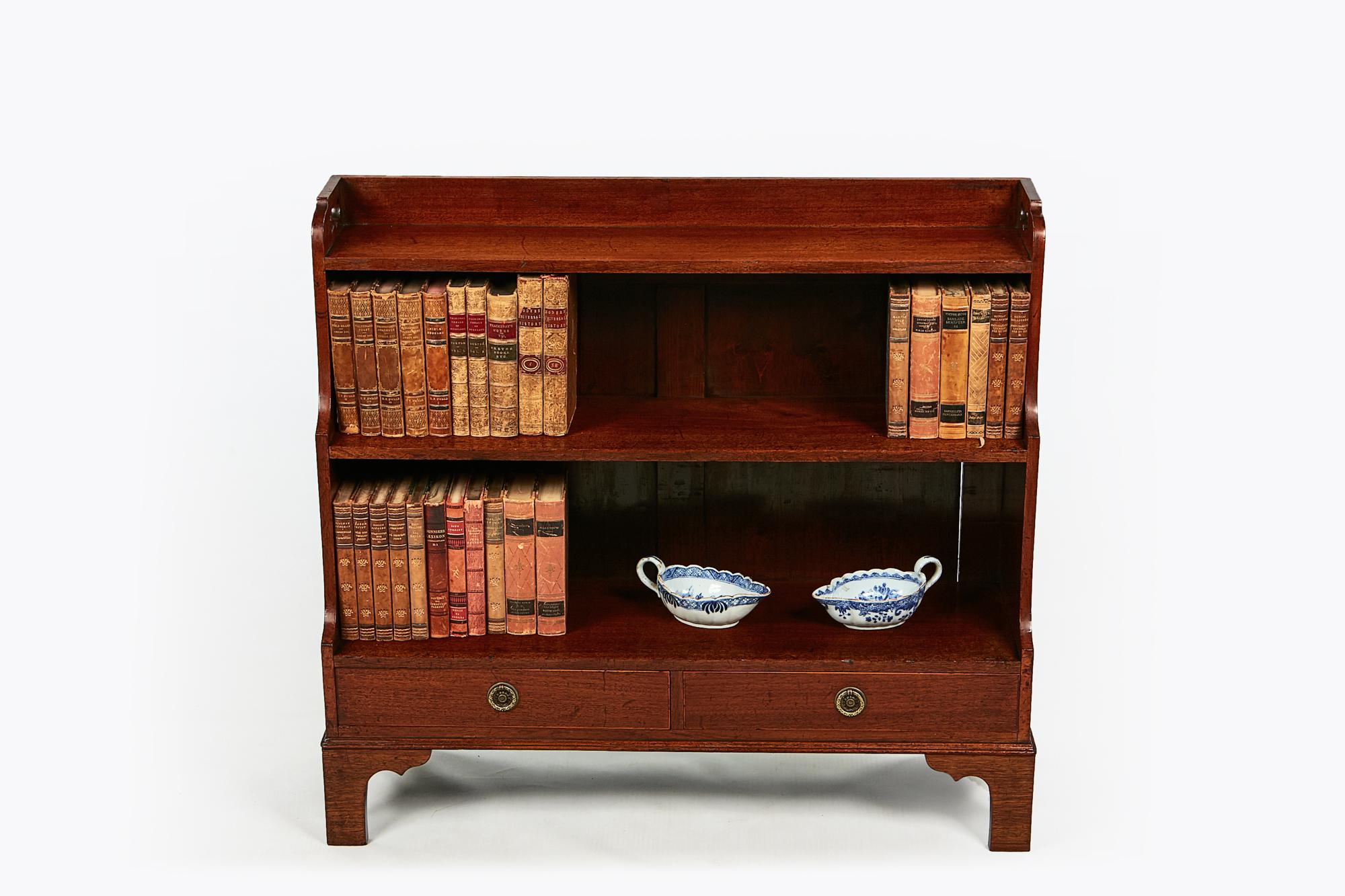 Early 19th century George III miniature mahogany waterfall bookcase. The shaped and moulded bookcase with heart shaped fret cut carrying handles over three graduated shelves raised on two short drawers with brass pulls terminating on ogee bracket