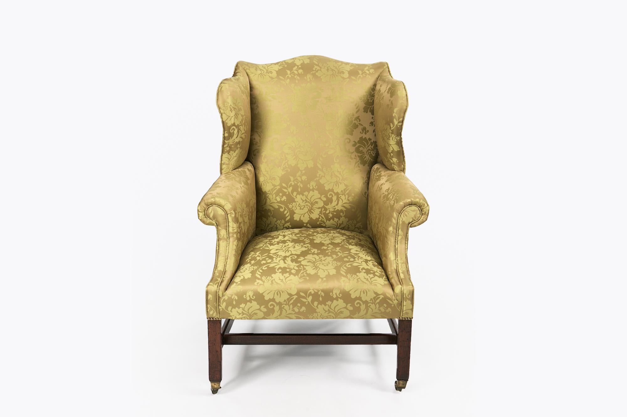 Early 19th century George III wing chair, the shaped back without scrolled wings and arms raised over squared leg joined with H stretcher terminating on brass casters.