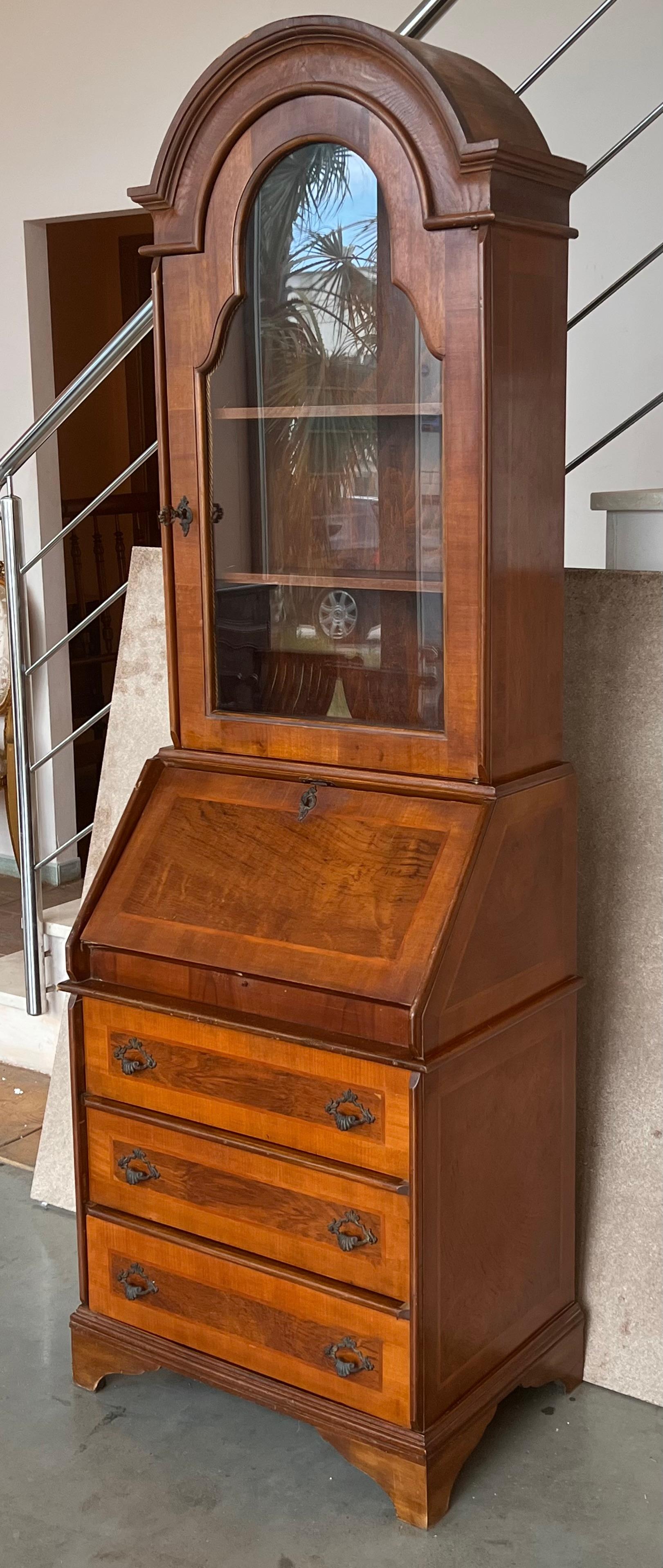 This is a charming George l style walnut diminutive secretary. The domed cornice over a conforming vitrine cabinet . The bottom section contains a drop-front opening to reveal a leather-inset writing surface and cubby holes above three long