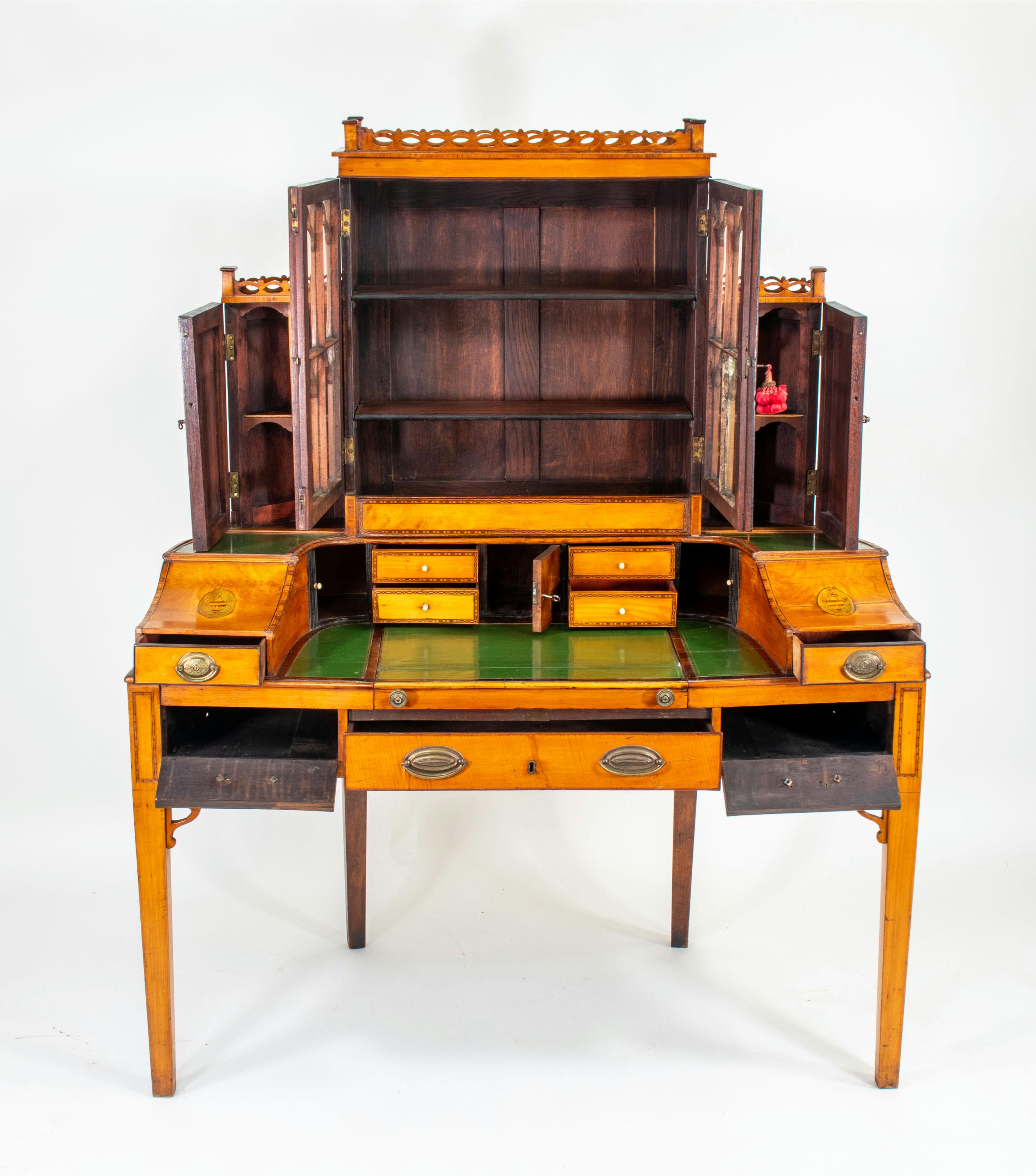 Este escritorio de madera satinada Jorge III de principios del siglo XIX ejemplifica la elegancia y la artesanía de la época con su diseño neoclásico. La pieza presenta un intrincado trabajo de marquetería, líneas curvas y refinadas decoraciones,