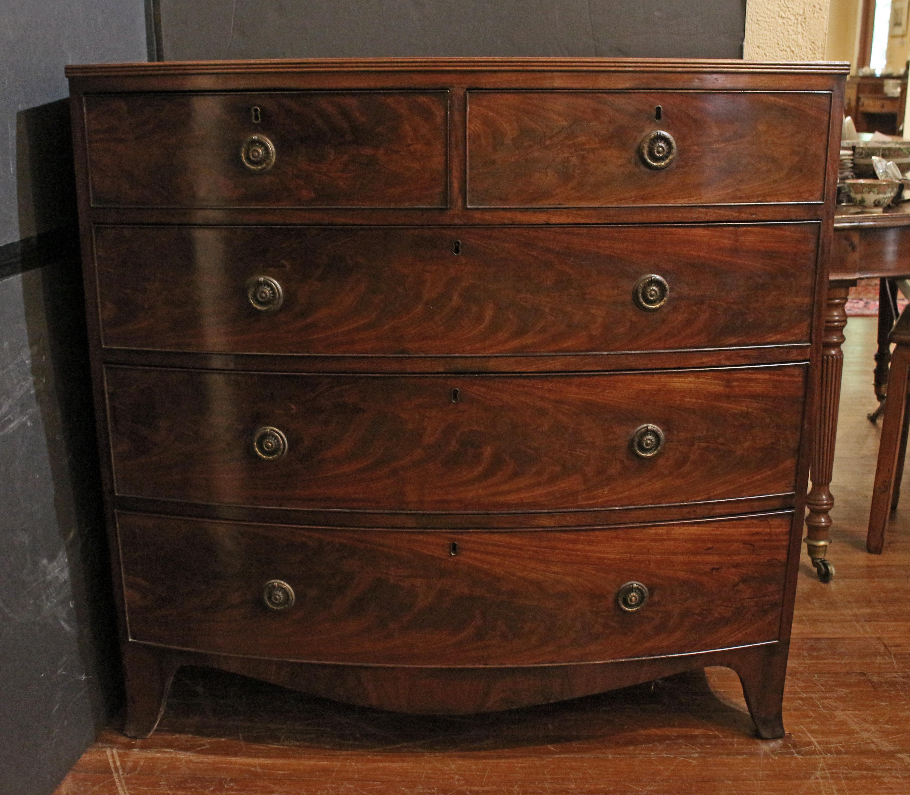 Early 19th century Georgian bowfront chest of drawers, English. Two short over three long graduated drawers. Mahogany. Raised on French splay feet. Shaped apron. Crossbanded top with reeded edge. Brass ring turned pulls. Mahogany & pine secondary