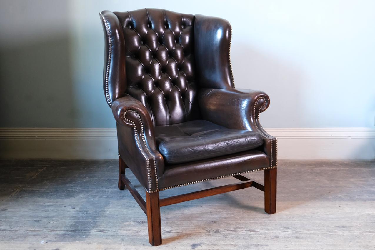 Georgian brown leather-upholstered wingback armchair, English, early 19th century. 

Fully restored Georgian brown leather upholstered wingback armchair. The button upholstered back and slightly bowed seat is outlined with a close nail trim and