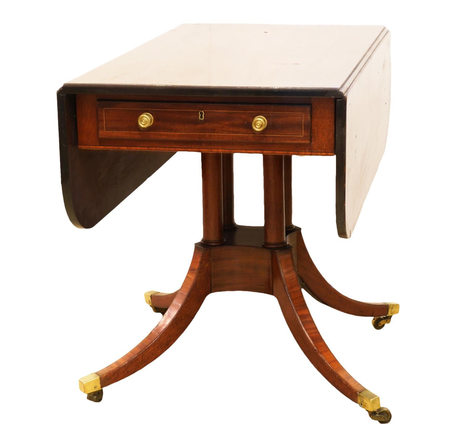 This English Georgian inlaid mahogany drop-leaf table feature a satinwood banded top above a string inlaid drawer resting on a four column pedestal and a base with four string inlaid splayed legs and brass castors. A very elegant piece of furniture