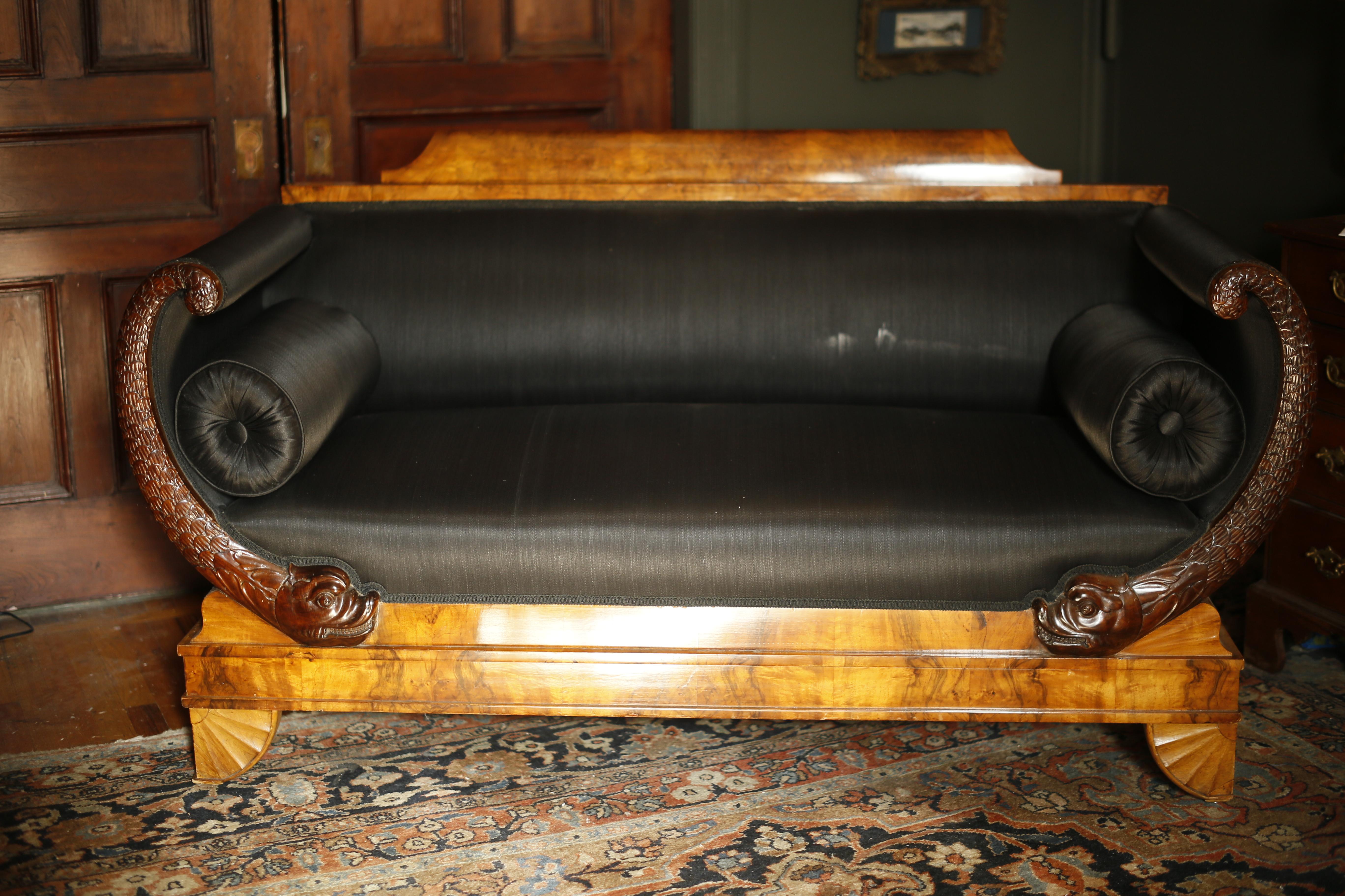 A magnificent piece of classical seating of ample proportions and fine detail. The couch frame is covered in beautiful burled walnut veneer and the arced arm supports are faced with stunning carved mahogany dolphins. The sofa is supported by a