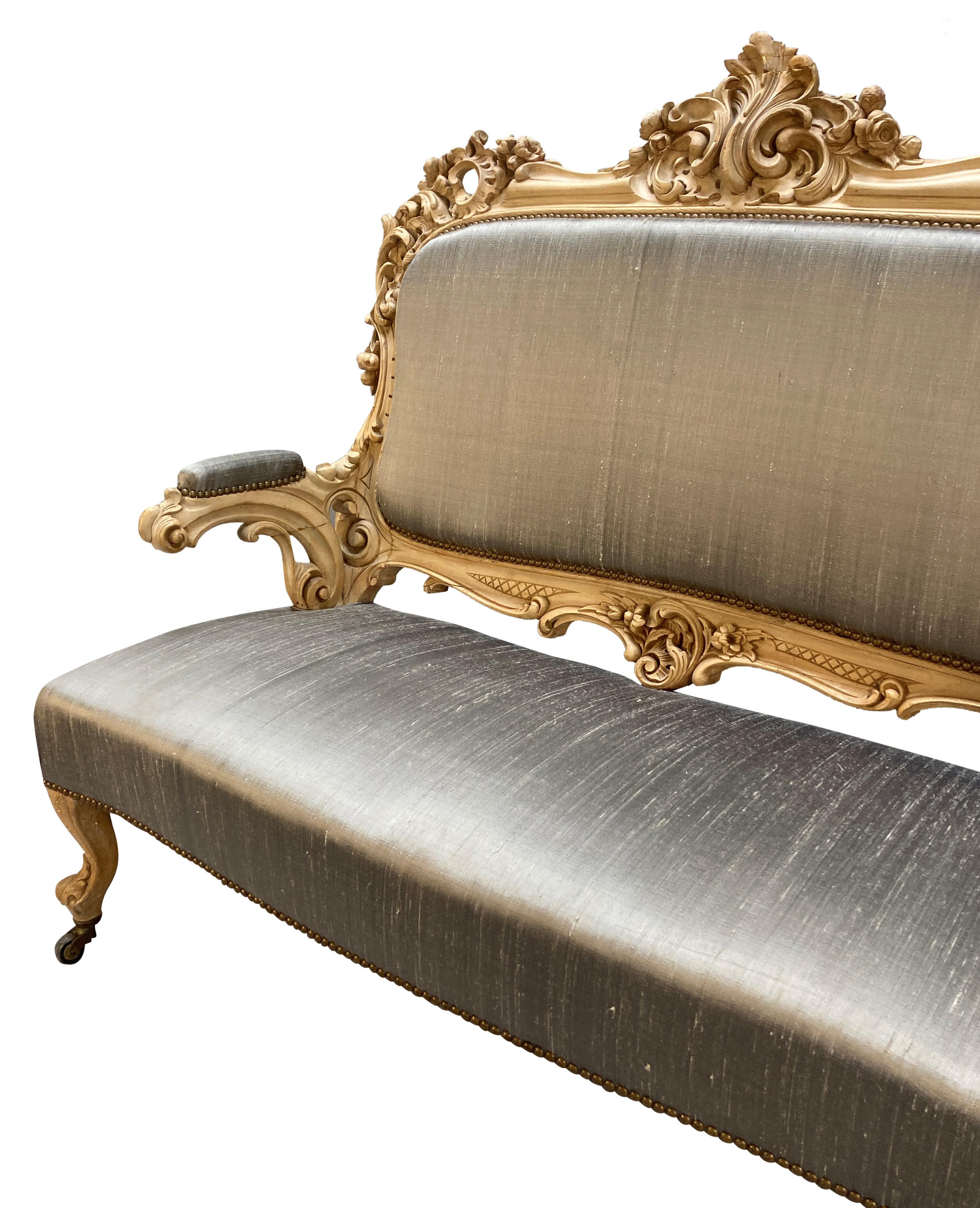 Divano tedesco dell'inizio del XIX secolo in stile rococò. In legno sbiancato intagliato e rivestito in seta color pietra con borchie e piedini in ottone.