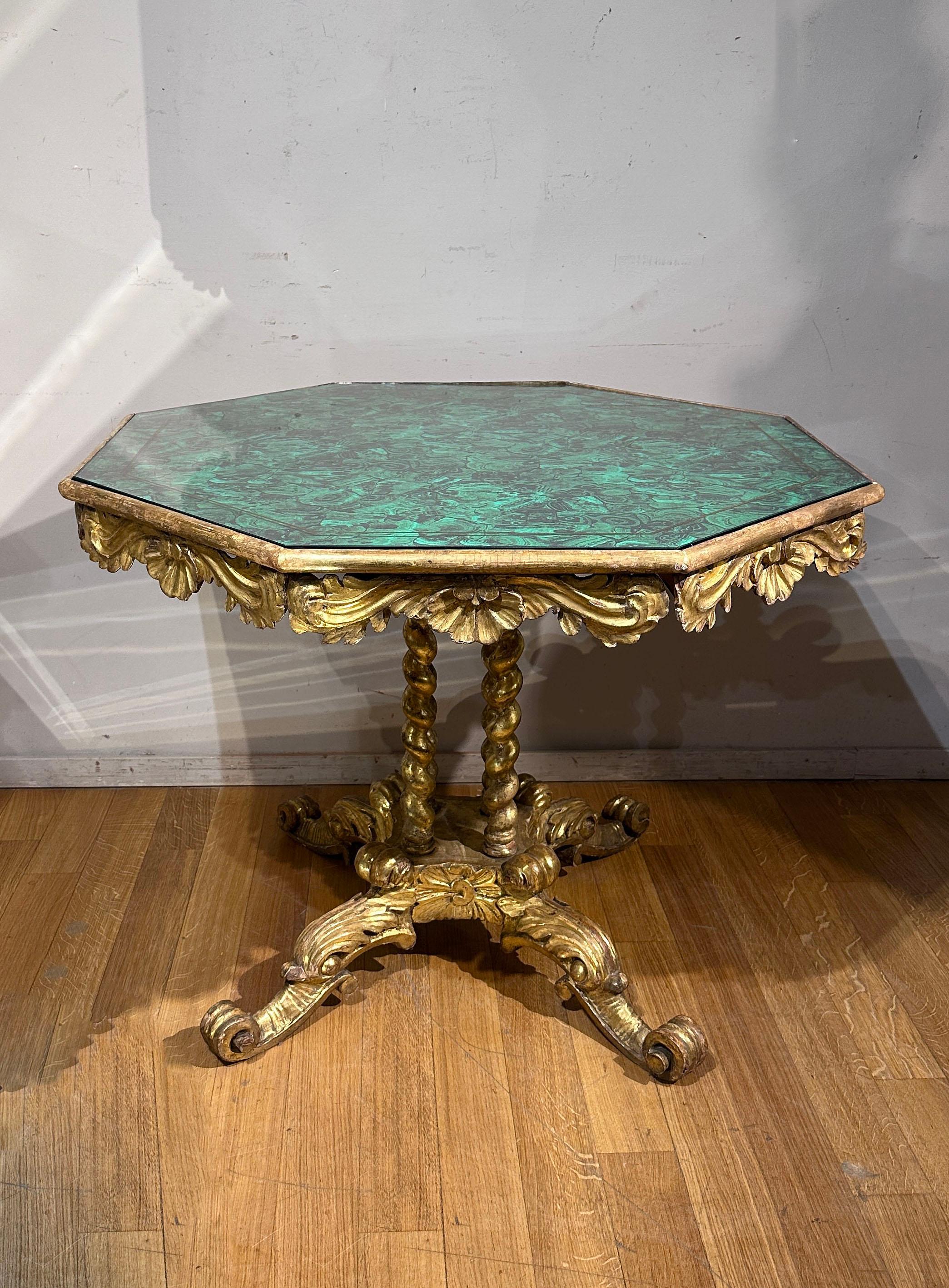 Cette table à thé, fabriquée en bois finement sculpté et ensuite dorée à la feuille d'or pur, est un authentique chef-d'œuvre de design et d'artisanat. Caractérisé par un plateau rond en tissu, élégamment protégé par du verre, il est une véritable
