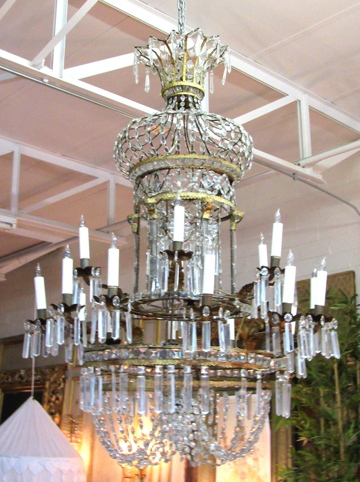 Gilt bronze and crystal Italian chandelier from circa 1790-1850, with two tiers of lights, six upper and twelve lower, supported by decorative candle branches with designs of stylized anthemion leaves. The candle branches attach to a large bronze