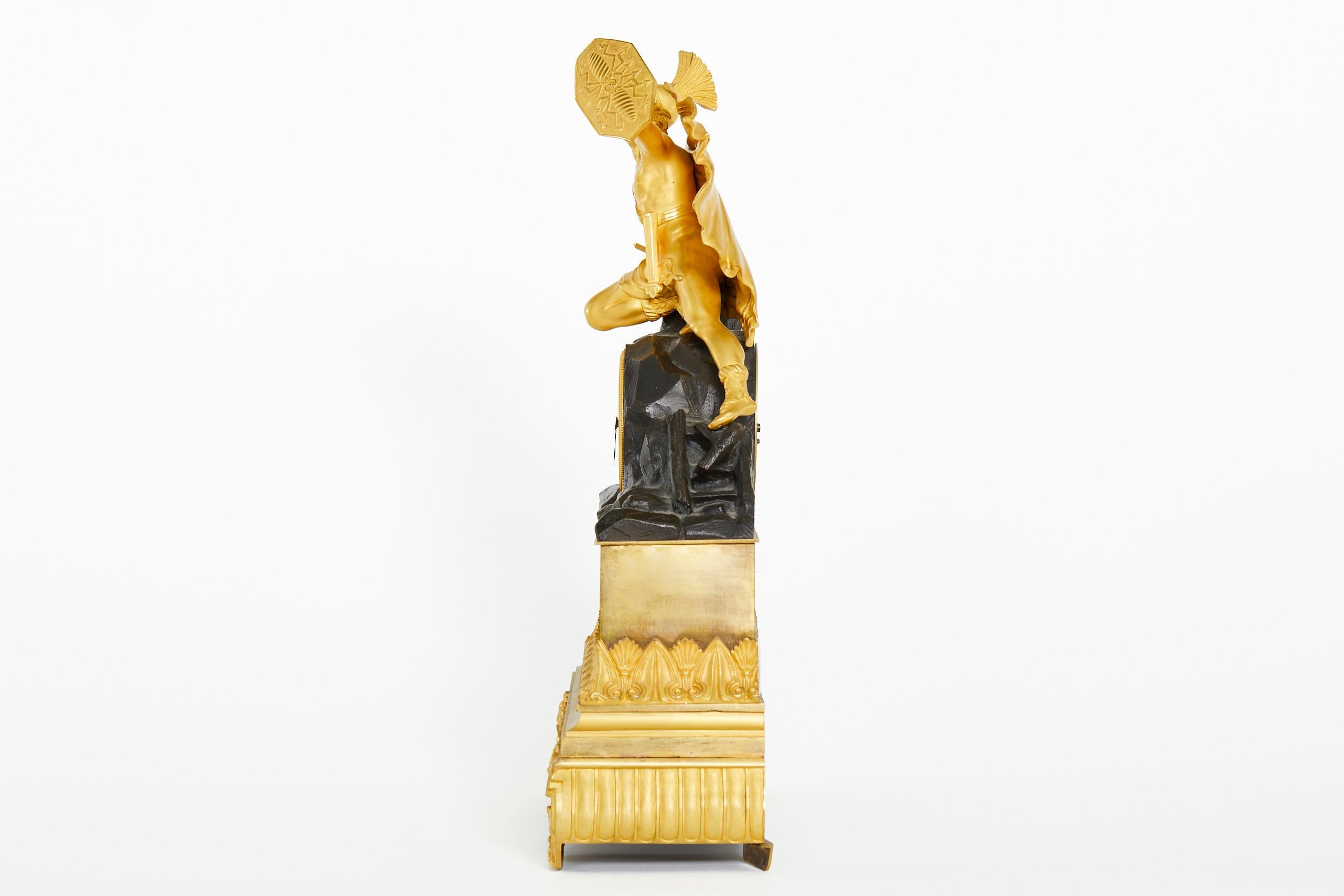 Pendule de cheminée du début du XIXe siècle, de style Charles X, en bronze doré et ornée de motifs figuratifs. L'horloge représente un soldat surmonté tenant un bouclier. Mouvement en laiton à ressort de huit jours, avec sonnerie à cloche et