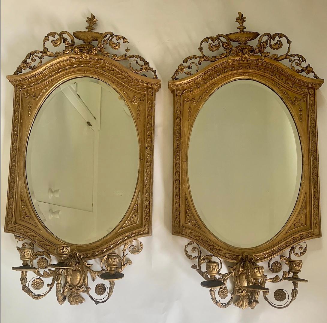 A stunning pair of early 19th century English gilt wood girandole wall mirrors. Each mirror has a triple candelabra with beautiful scrollwork to the base and top, culminating in an Adam-style urn finial. The detail on the frames is intricate and of