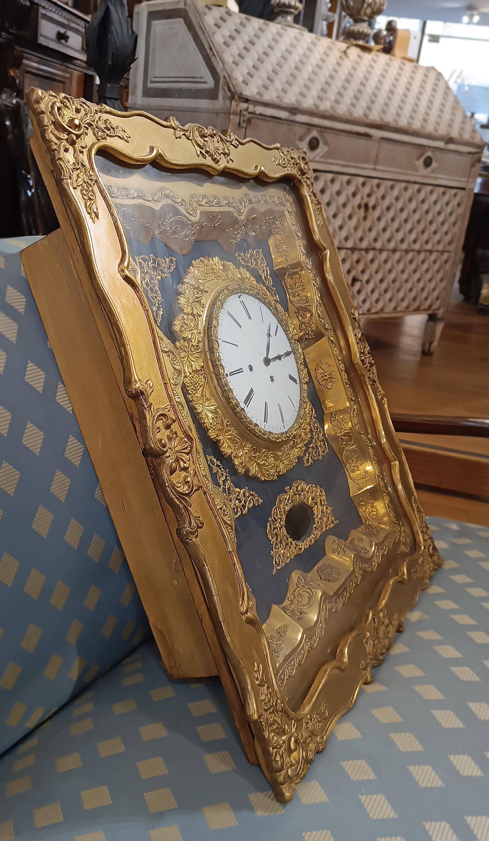 Splendid wall clock set in an elegant opening wooden case, with carved frame and golden tablet. The internal finishes of the clock are also in golden tablet and brass. The decorations, rich in garlands and intertwined plant motifs, add a touch of