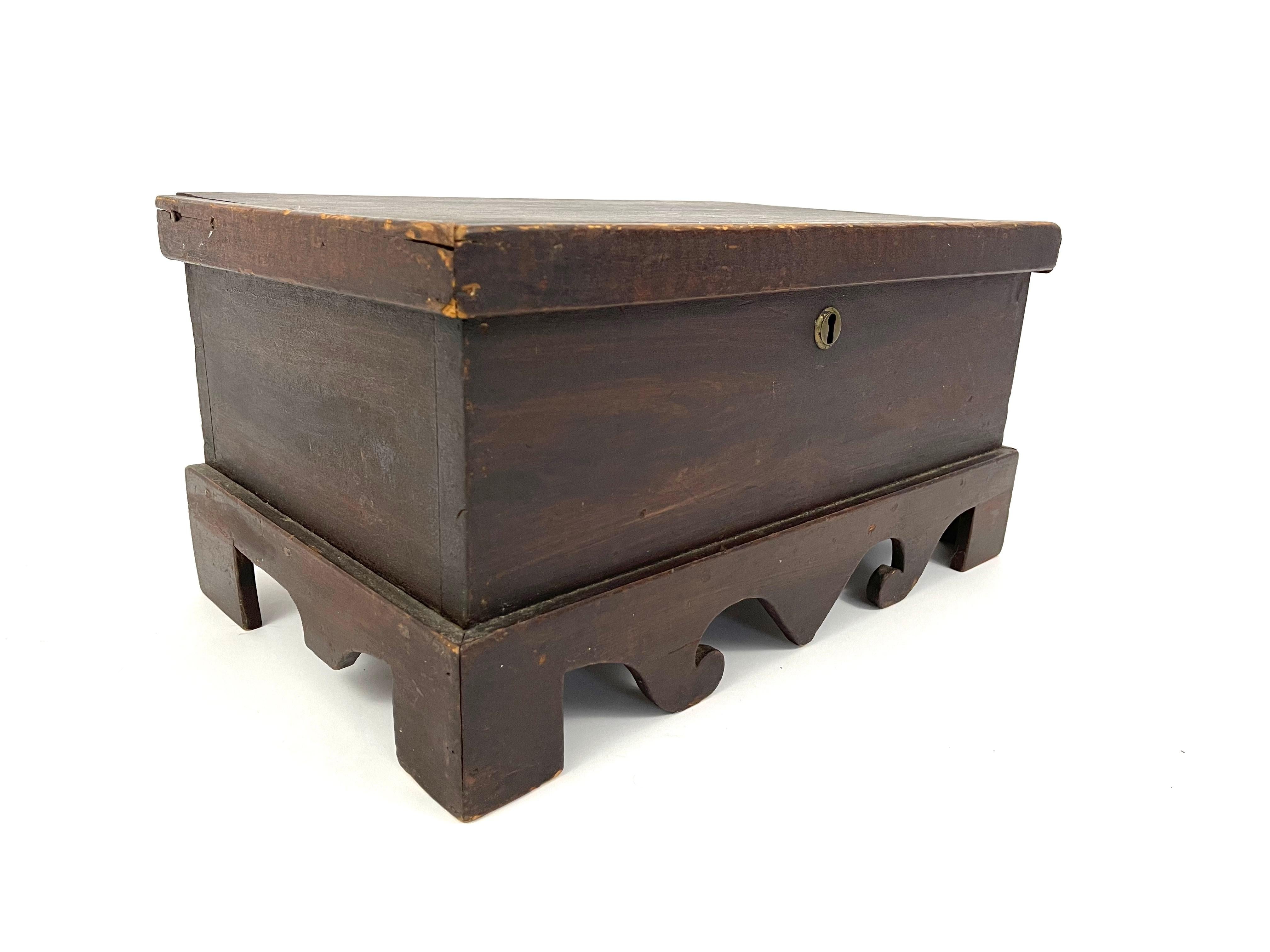 An unusual and sculptural early 19th century grain painted pine box, of rectangular form, with lift top lid, attached to a base with bracket feet and whimsical scrolled cutout decoration (like an inverted swan's neck pediment). Wonderful old, dry