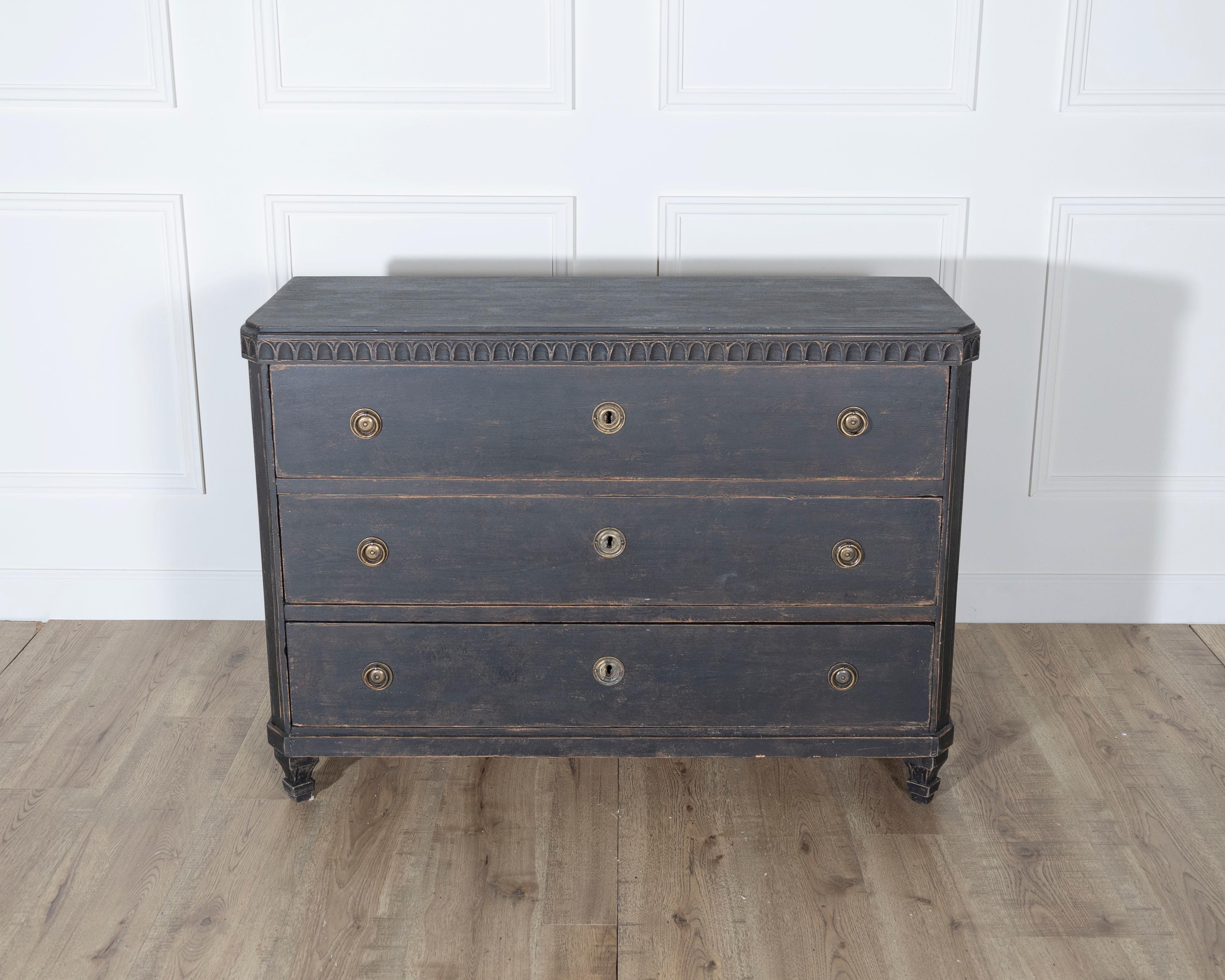 A stately Swedish Gustavian chest of drawers dating to the early 19th century, featuring classic neoclassical restraint paired with subtle decorative flourishes. Crafted in solid pine and painted in a deep, dry black, the piece showcases a