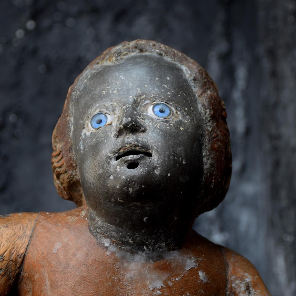 We are proud to offer a very rare and unusual example of an early 19th century hand carved section wood putti figure with a black lead face and glass eyes. A unique form depicting an angelic religious figure, the lead face and blue glass eyes is