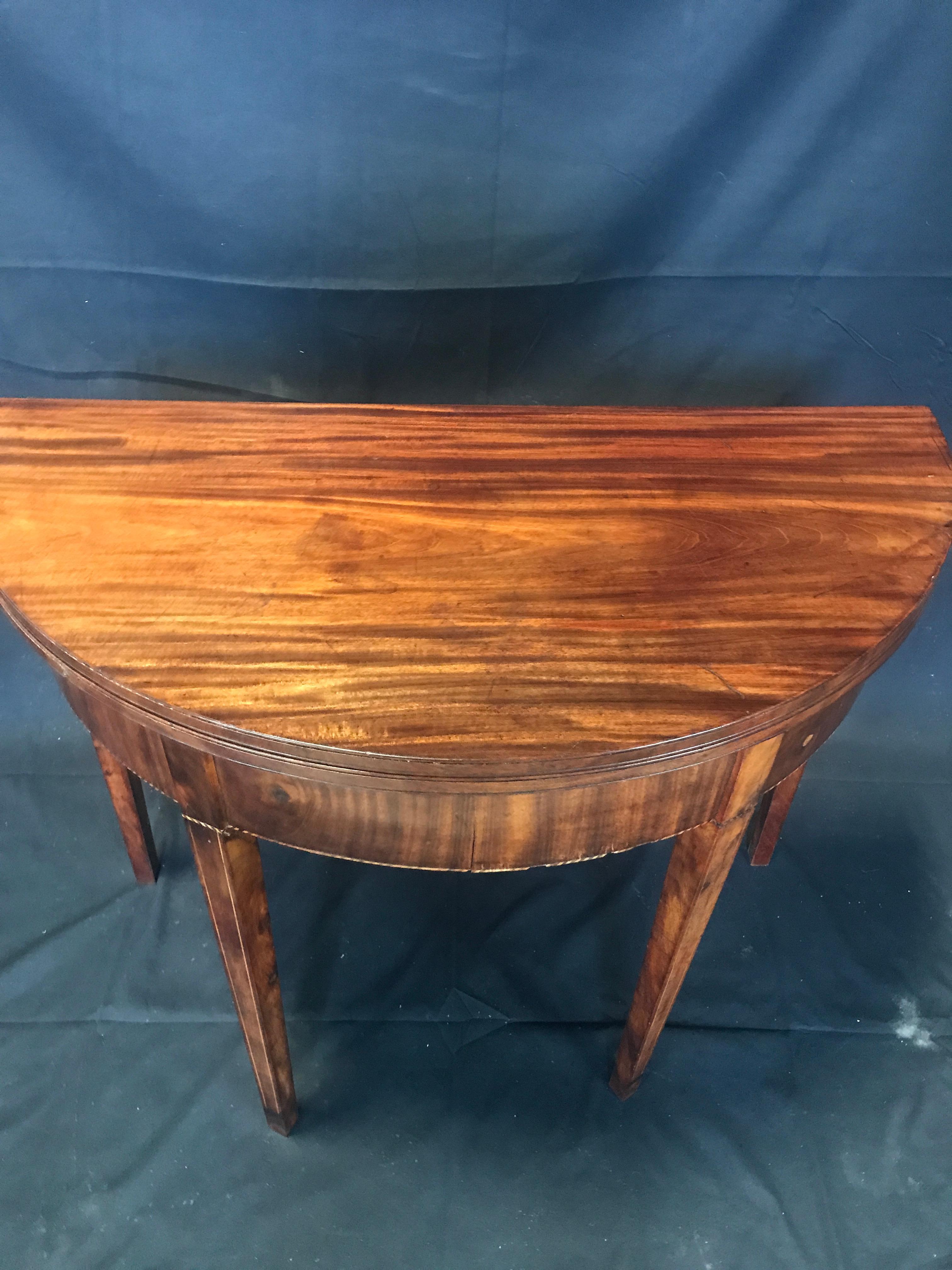 This super early American Hepplewhite inlaid mahogany card table in demilune shape is dated 1810-1815. Back leg swings out in typical game table function to support top when open.
#2385

Measures: H skirt 22.5” H open 27.5” W 35.5” D closed