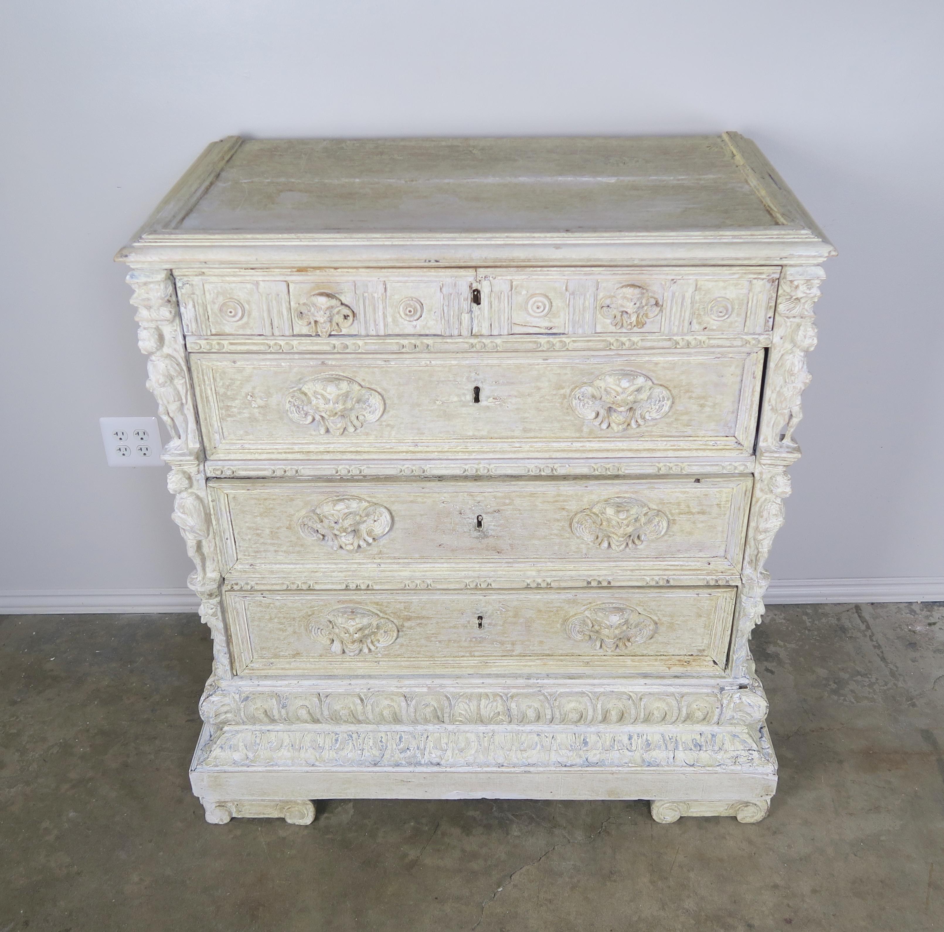 Early 19th century, possibly 18th century Italian carved chest with four drawers. The drawers are detailed with intricate hand carved face shaped pulls. The chest is beautifully worn with a white wash finish. The piece stands on four capital shaped