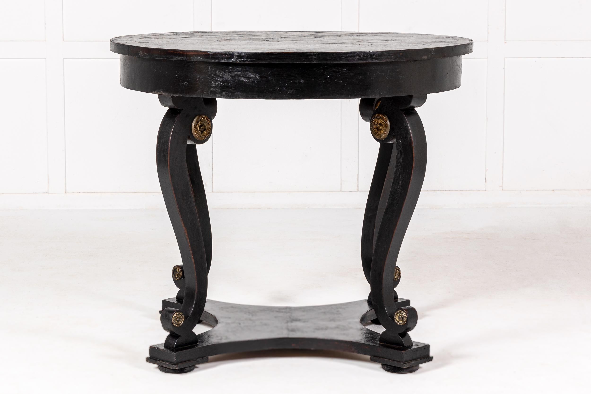 An Early 19th Century Italian Rustic Ebonised Centre Table.

Ebonised throughout with gilt metal or ormolu paterae to the tops and bases of each of the scrolling supports. The piece has flattened bun feet supporting an quadripartite platform