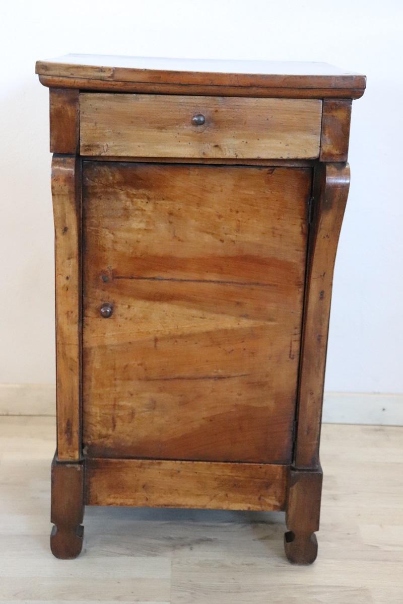 Lovely antique Italian nightstand of the period Empire, early 19th century in solid walnut wood. The nightstand very refined linear and elegant with on the front two decorative columns. On the front one-drawer and one-door, internally available a
