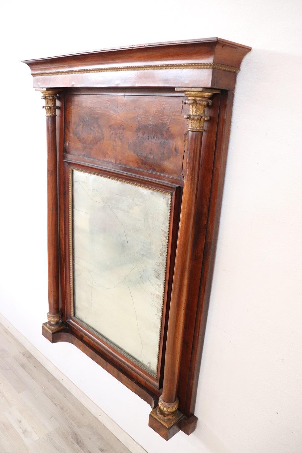 Beautiful elegant antique Empire wall mirror, 1800s walnut wood hand carved with finely decorations. Elegant carved and gilded decorations. On the sides two columns with gilded corinthian capitals. The mirror is original antique mercury. The