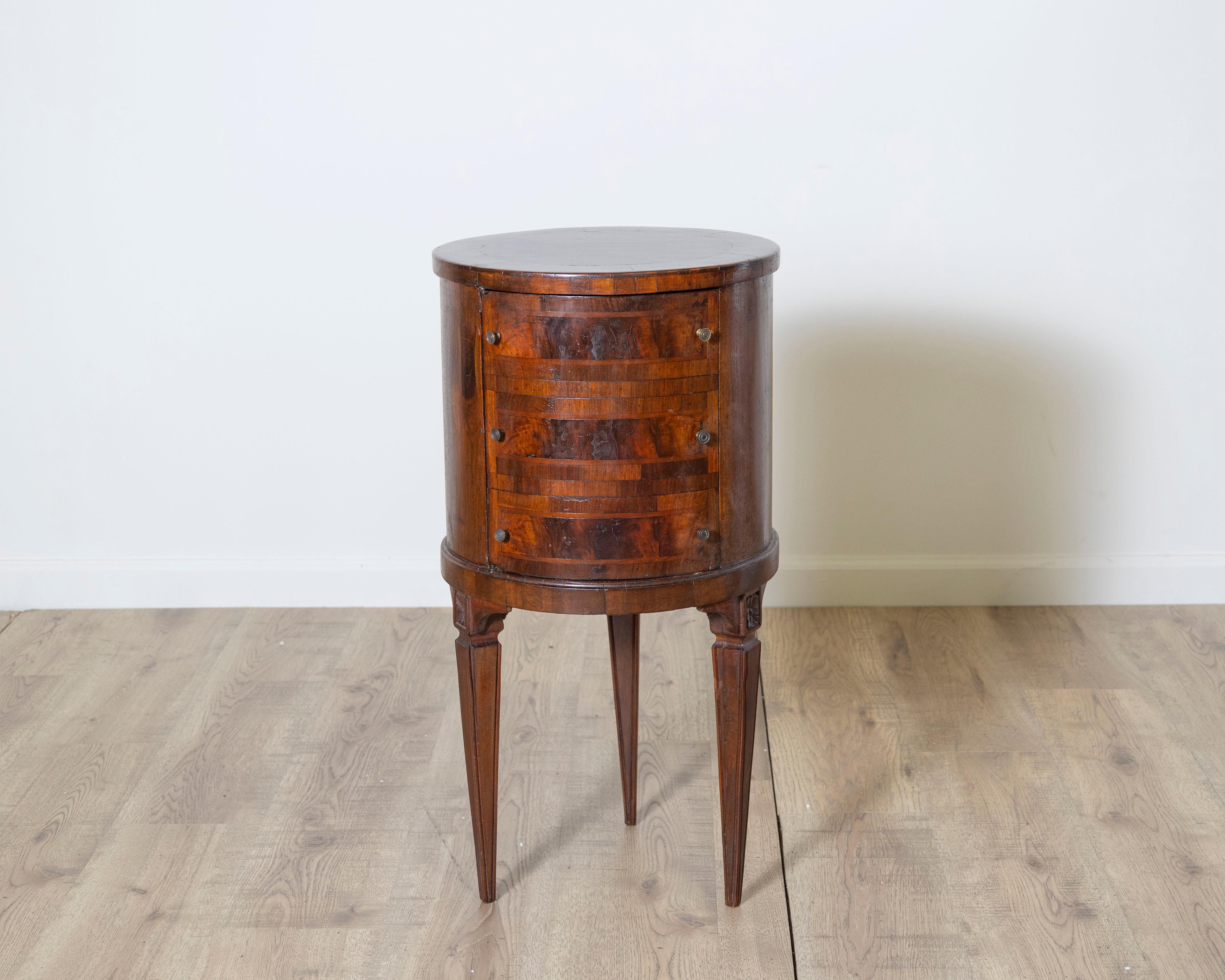 A rare and charming circular cabinet in the Louis XVI style, crafted in rich threaded walnut with elegant proportions and finely tapered legs. The cylindrical body features a subtly inlaid façade with decorative banding and a concealed door that