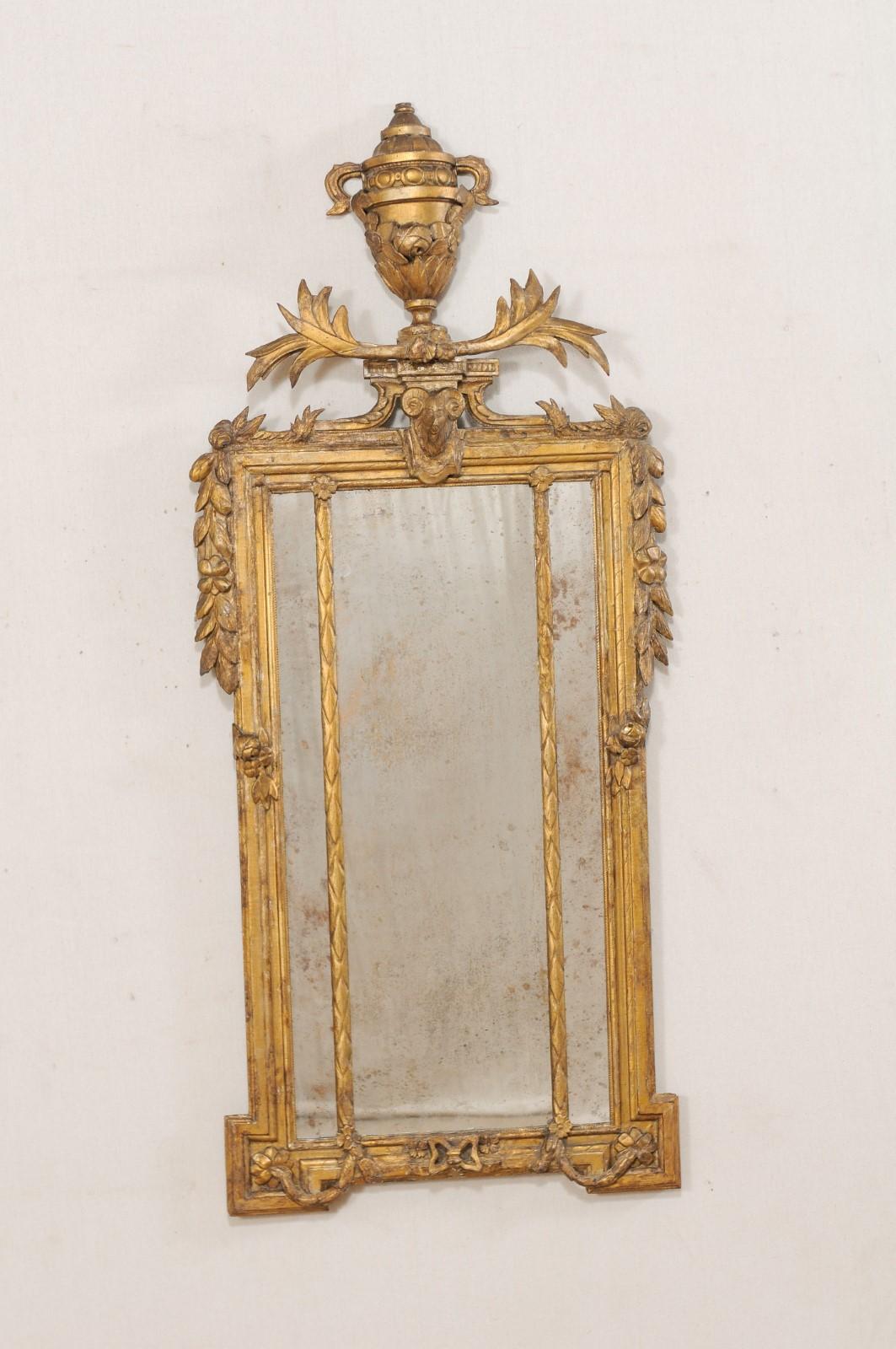 An Italian neoclassical gilt and carved wood mirror, circa early 1800s. This early 19th century neoclassical mirror from Italy features a richly carved giltwood surround topped with a raised urn crest, spewing leaves, and ram's head carved beneath,
