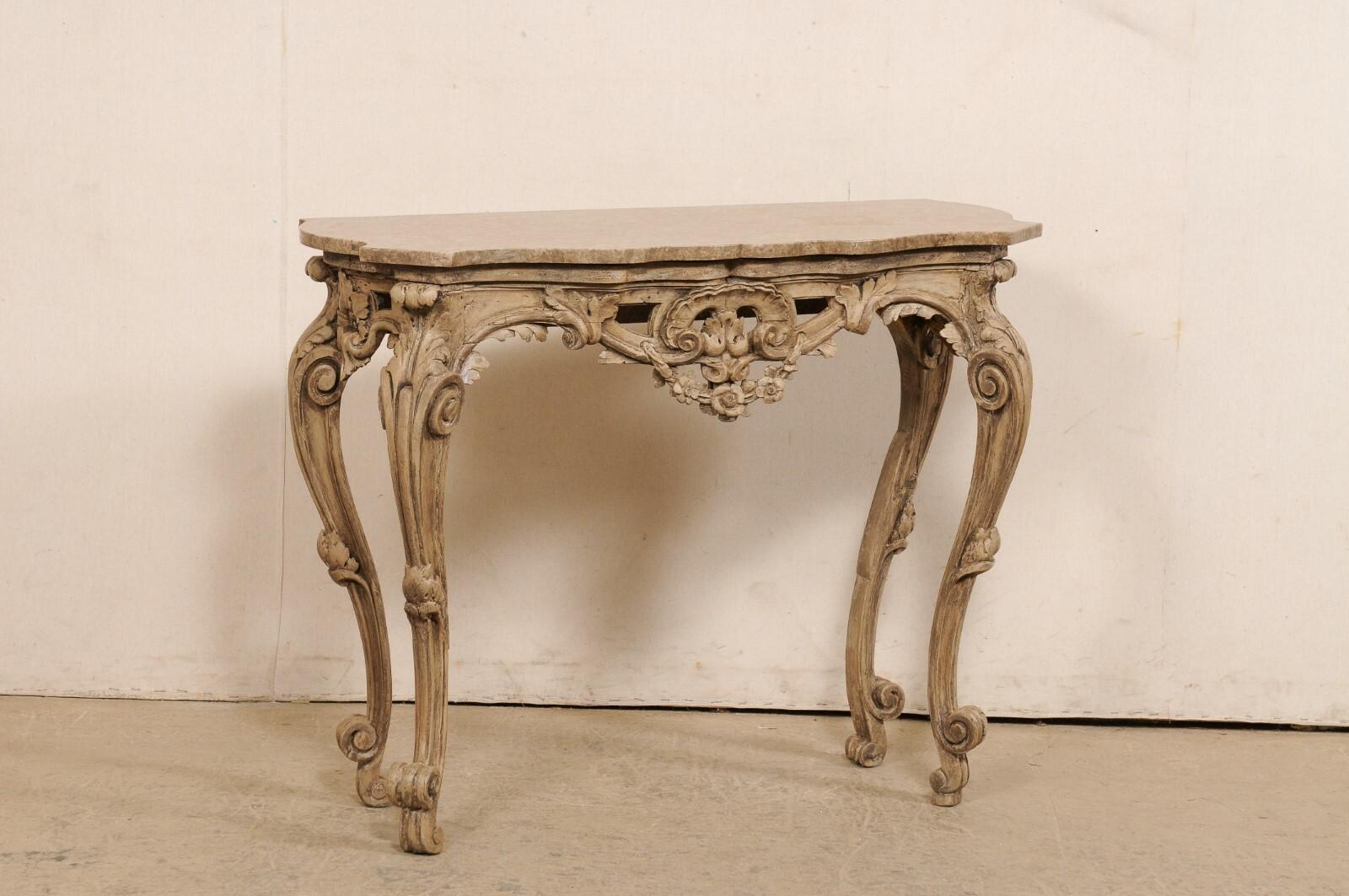 An Italian Rococo style carved wood console table with marble top from the early 19th century. This antique table from Italy has a shapely cut marble top along front-side, with canted front corners and a flattened backside (as made to rest against a
