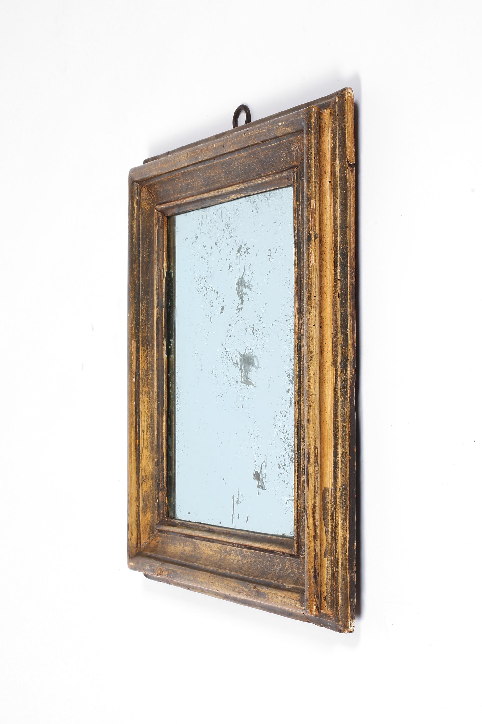 Charmant miroir en bois sculpté de Toscane datant de la fin du XVIIIe siècle ou du début du XIXe siècle. Magnifiquement patiné avec des restes de dorure historique, il a conservé son anneau de suspension en fer forgé et sa plaque de verre au