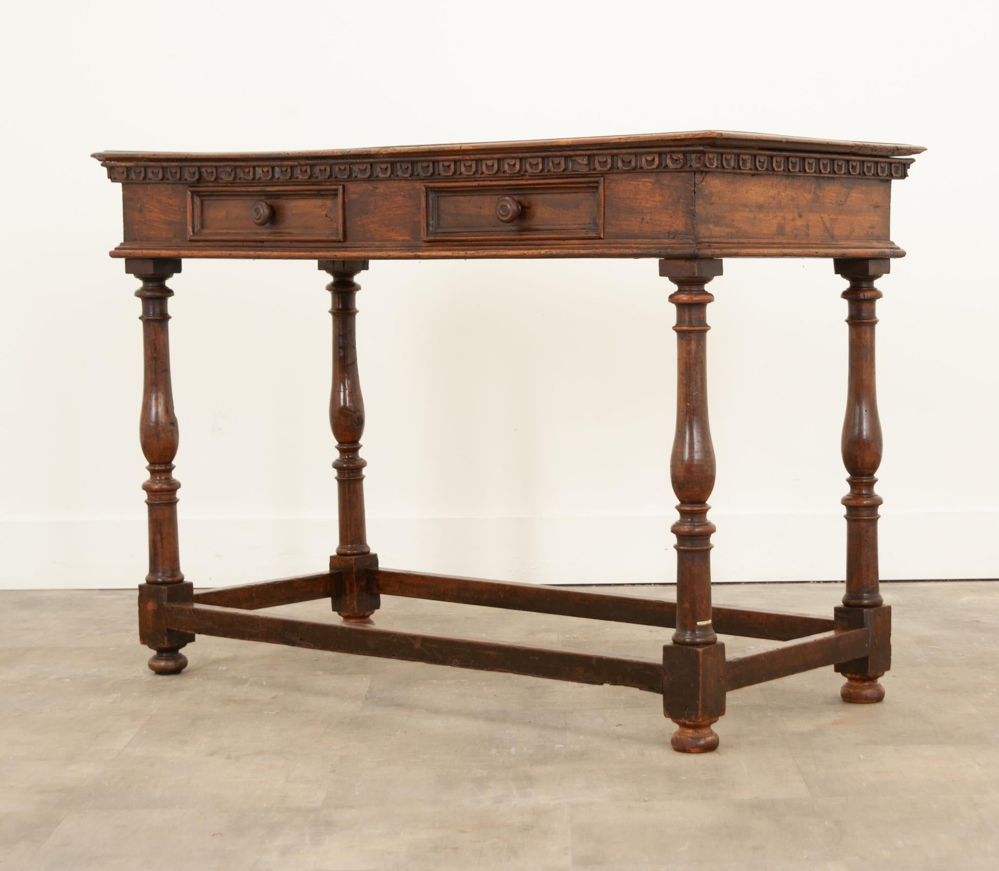 A handsome Italian walnut console table from the early 19th century with decoratively carved molding, turned baluster legs, plain side stretchers and bun feet. Created in Italy circa 1820, this walnut console table features a rectangular top with