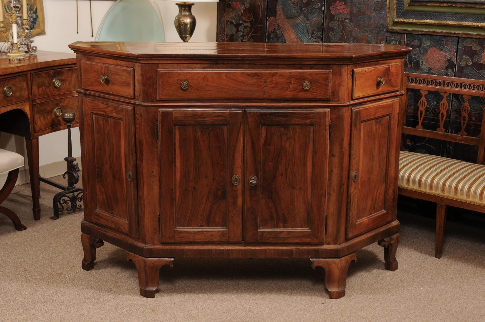The early 19th century Italian credenza in walnut with canted sides, 3 drawers with brass pulls and 4 paneled doors below terminating in shaped feet.