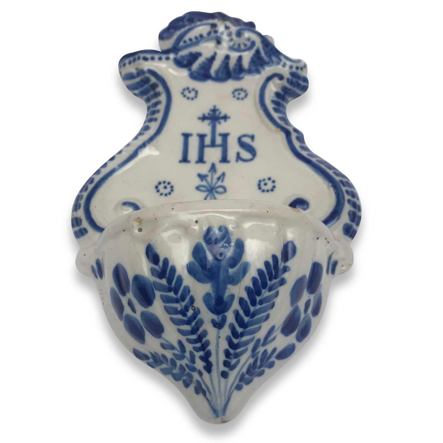 Antique shaped Holy Water font from Italy, a white and blue ceramic artwork dating back to early 19th century. 
This lovely religious work is decorated with blue vegetal and floral motifs on the font, the IHS central inscription and a cross in the
