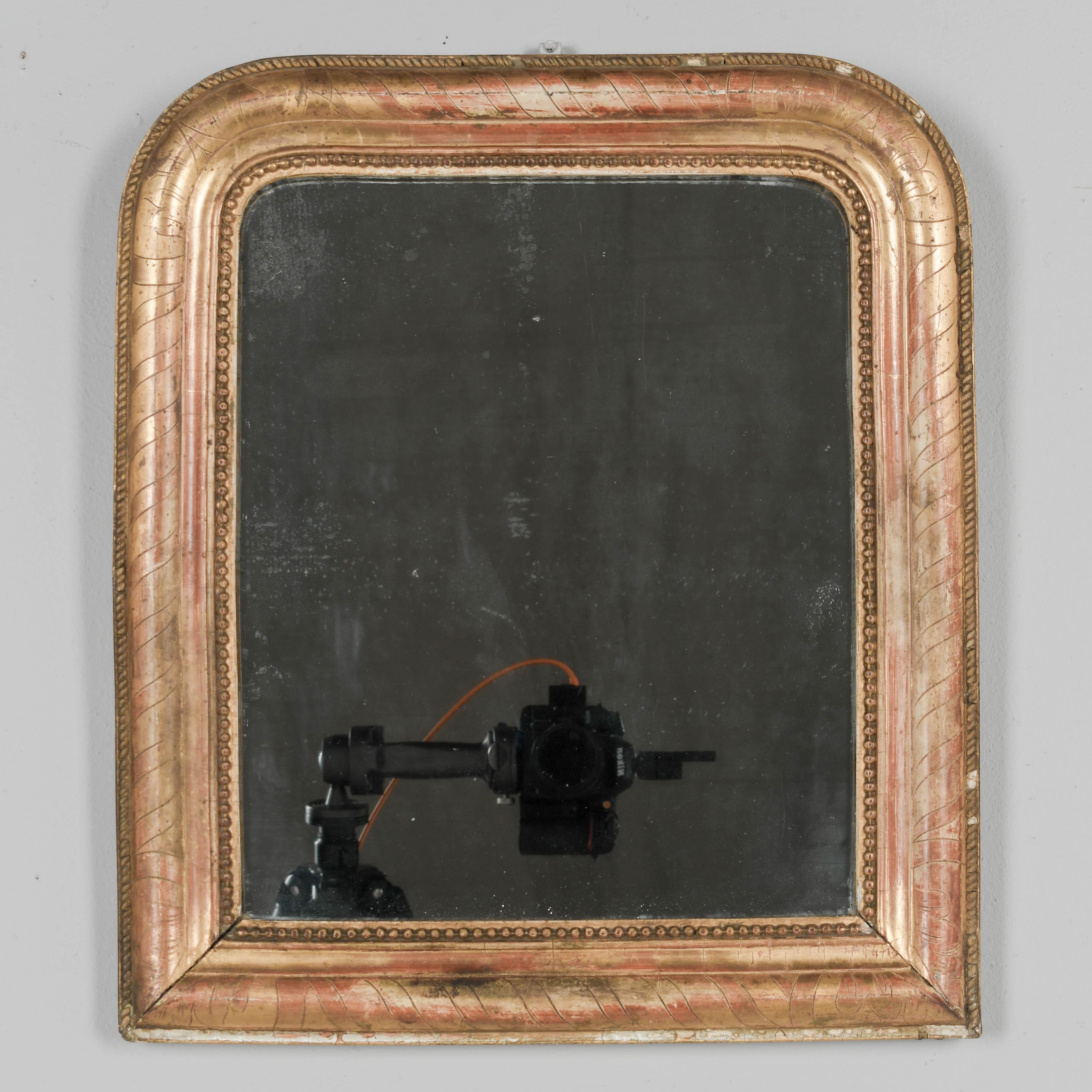 An early  19th century French Louis Philippe gilded small mirror with curved top corners, incised decoration and bead border. Warm gilt finish with red under rub exposed. Original mirror with mercury silvering. Minor gilt loss, and missing some