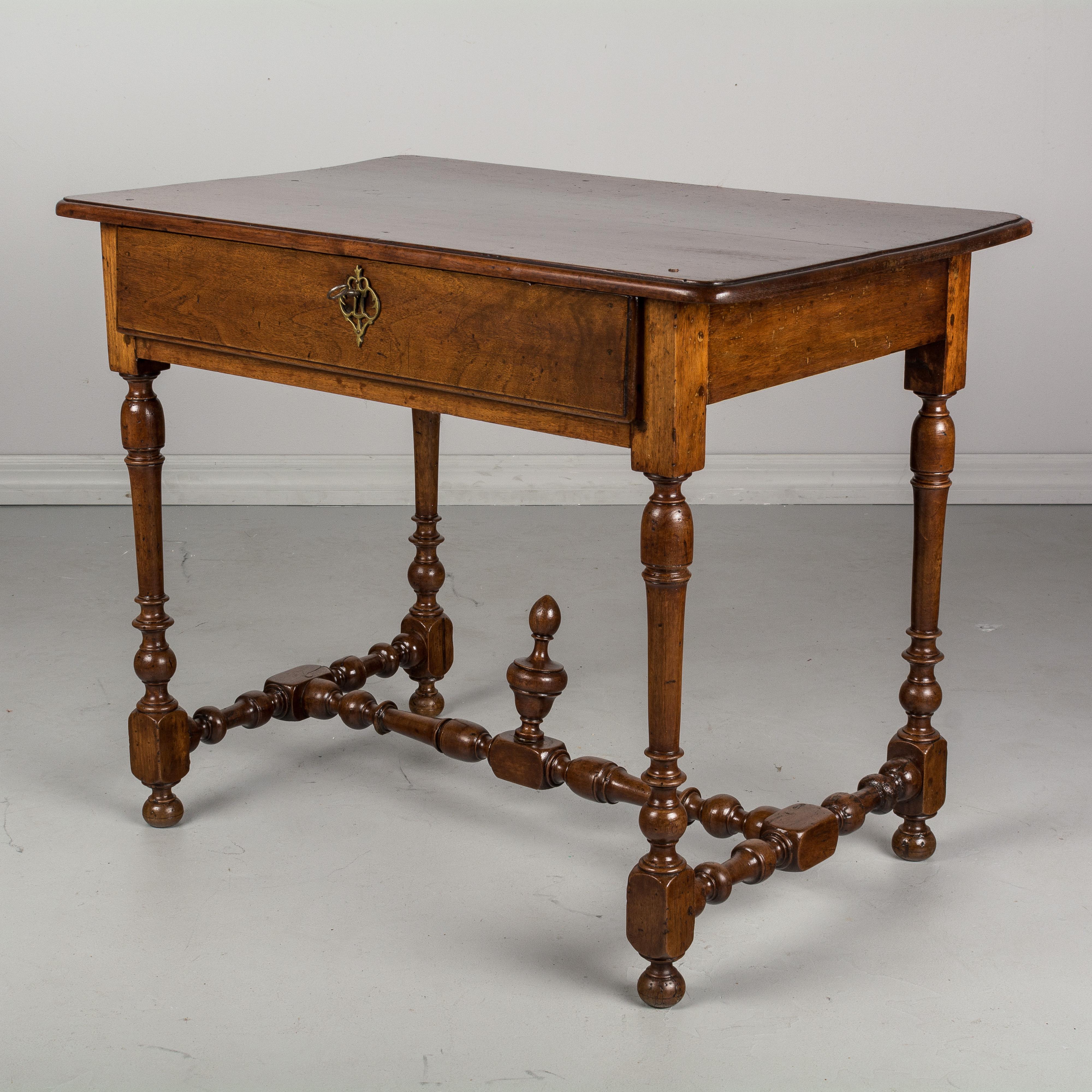 An early 19th century Louis XIII style French side table made of solid walnut with a large dovetailed drawer. Fine turned legs and stretcher with finial. Top is made from a single plank. Lock and key are present, but not in working order. Pegged