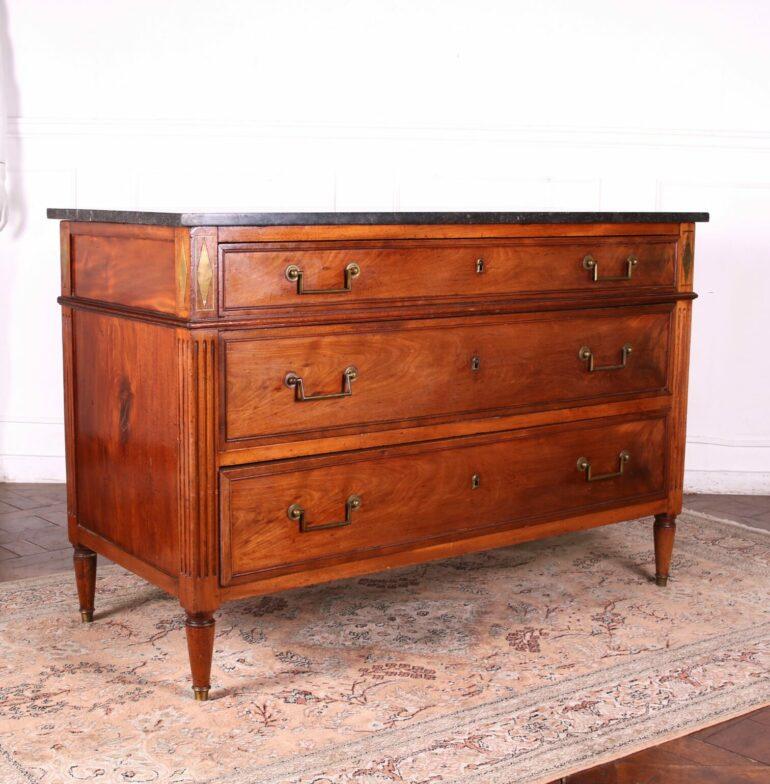 Early 19th Century Louis XVI style, walnut commode with brass inlays and a black Marble Top. Fronted by three large storage drawers with pairs of brass pulls.