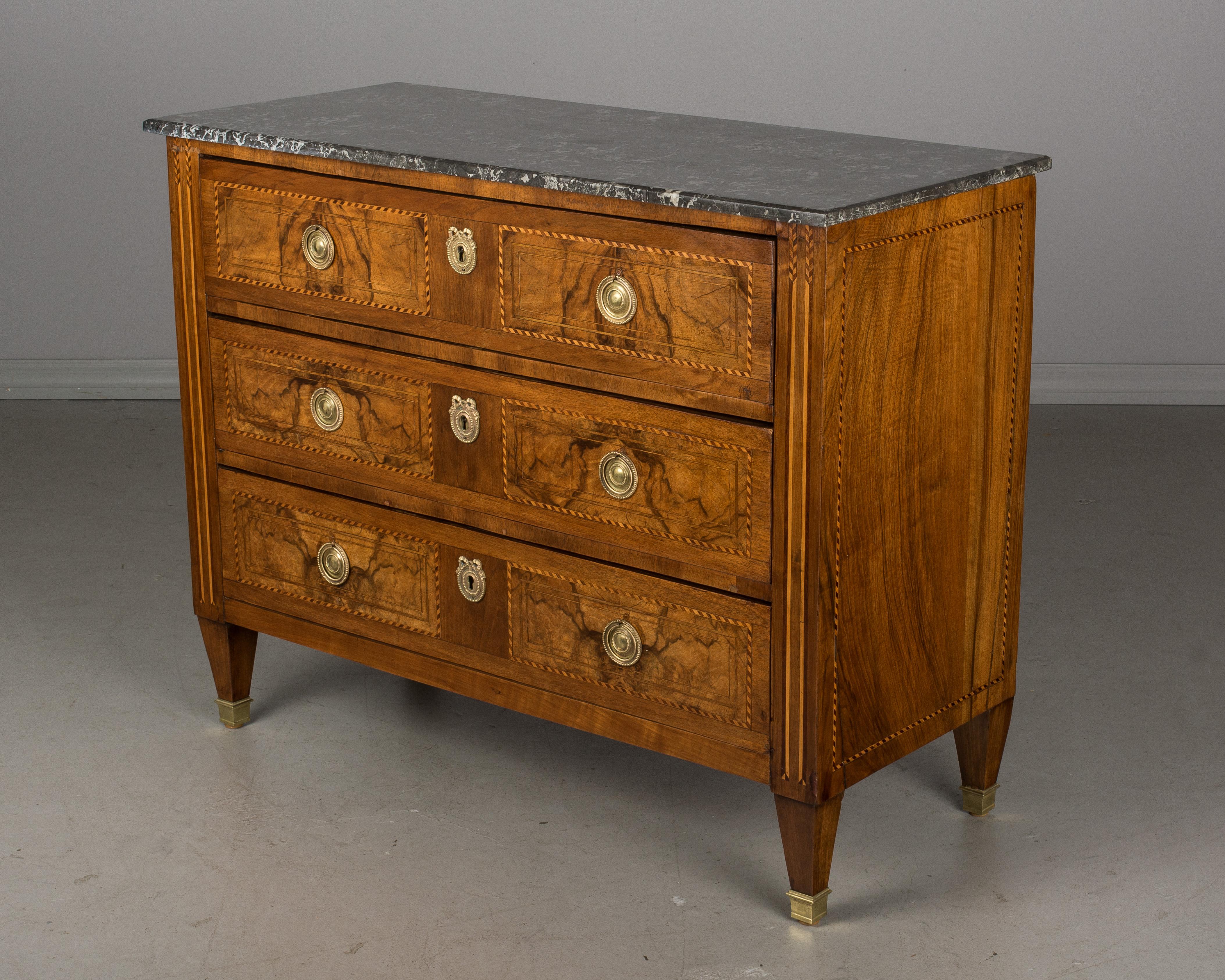 An early 19th century Louis XVI style marquetry commode with three dovetailed drawers and grey St. Anne marble top. Made of solid walnut and veneer of walnut and inlaid with various woods. Original brass hardware. Locks are presents, but there are