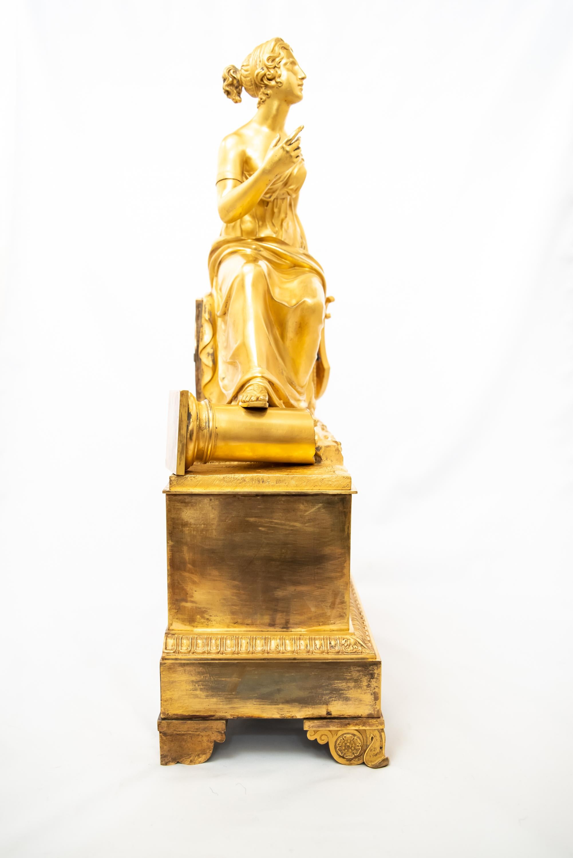 A gorgeous fire-gilt bronze clock depicting Madame de Staël seated in a classical landscape holding a lyre, and, at her feet, a fragment of a column. From the French “Restauration
