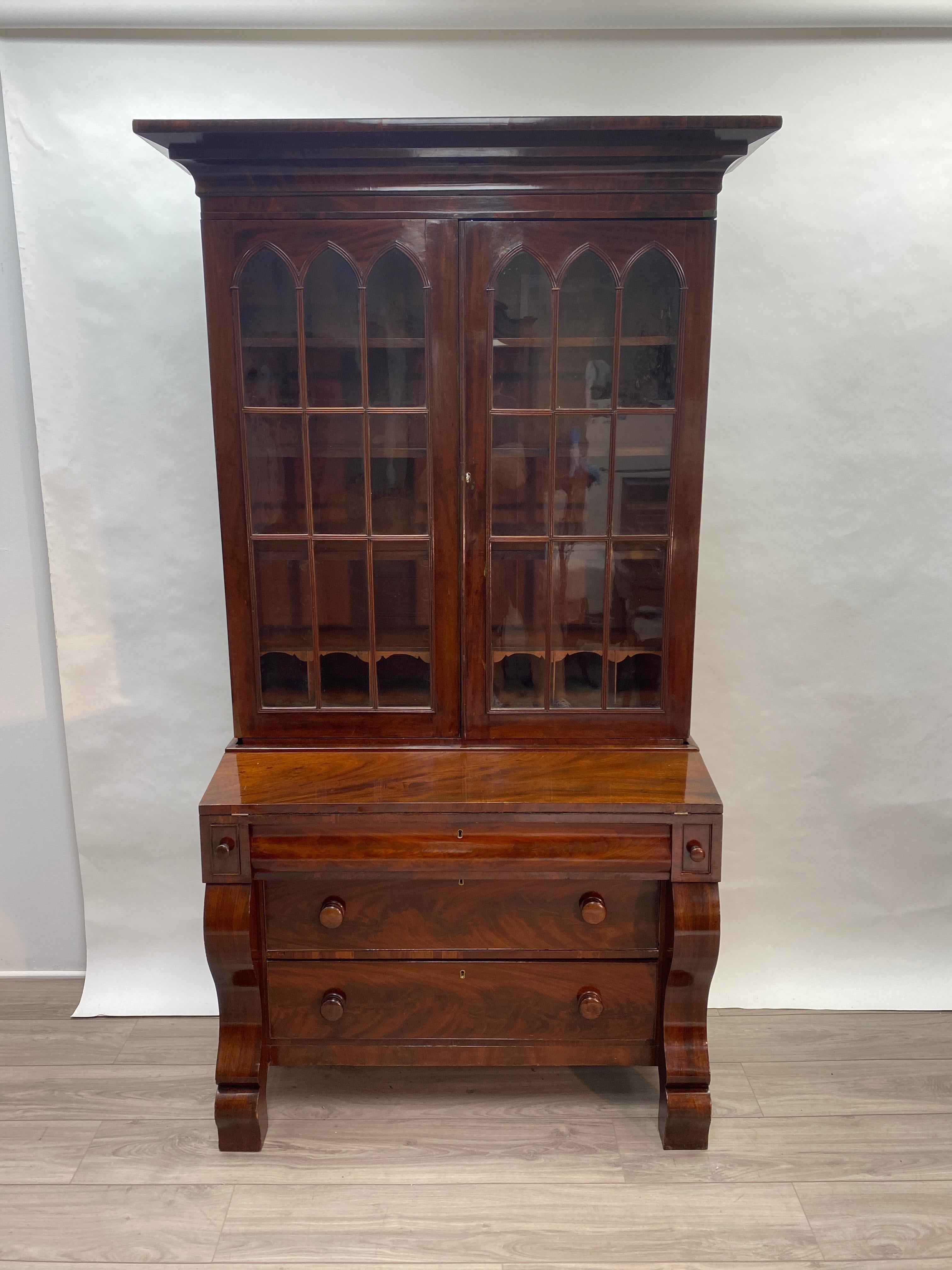 Early 19th century American Empire secretary with bookcase Circa 1840
Highly polished flamed mahogany case with three drawers resting on turned rear feet and ogee bracket feet. The top secretary is fitted with four interior shelves, pigeon holes