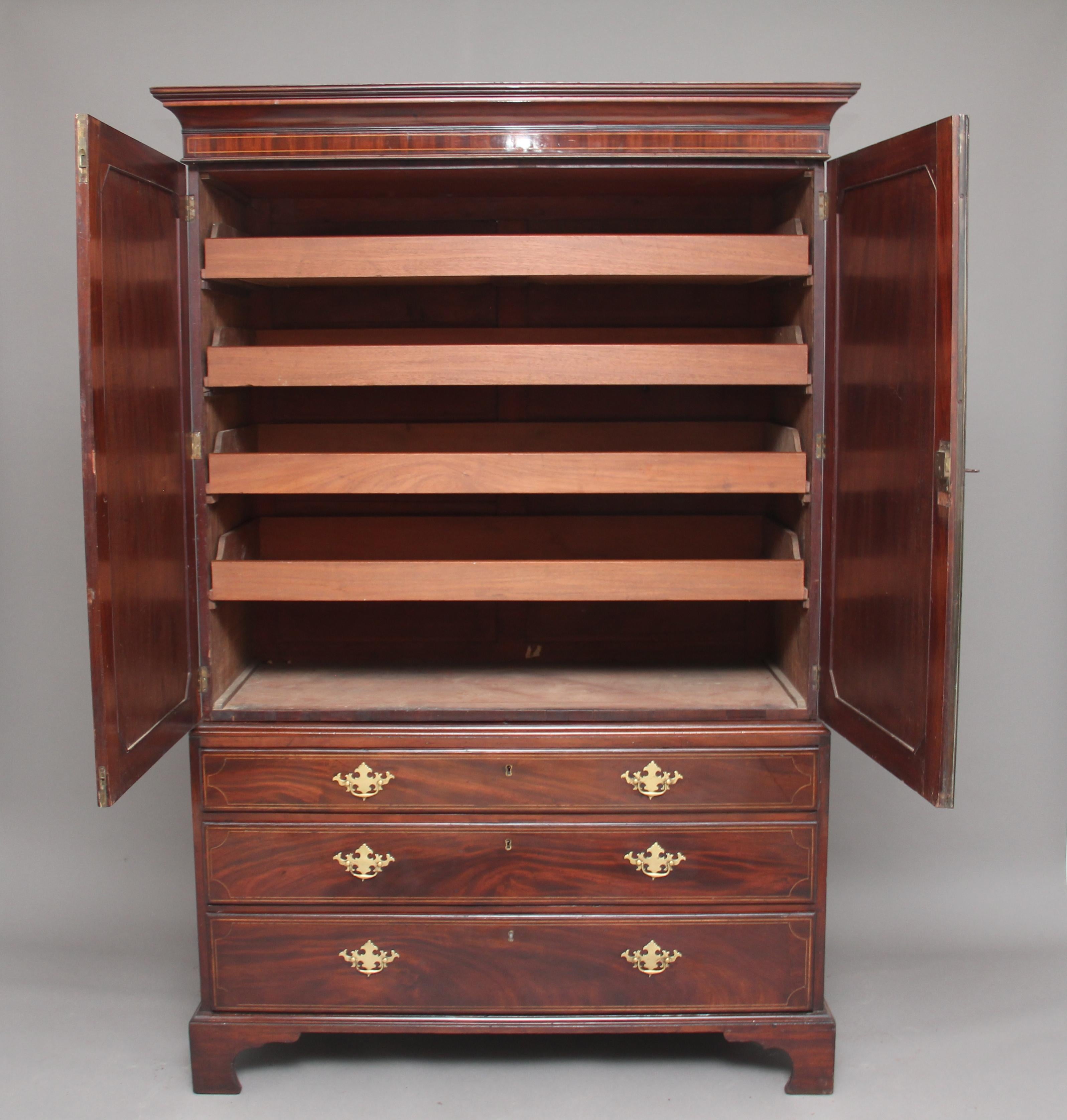 Early 19th century mahogany and inlaid press cupboard, with a stepped moulded cornice above a two door cupboard, the doors opening to reveal four pull-out trays / drawers, the door fronts inlaid with boxwood lines, urns, swags and floral decoration