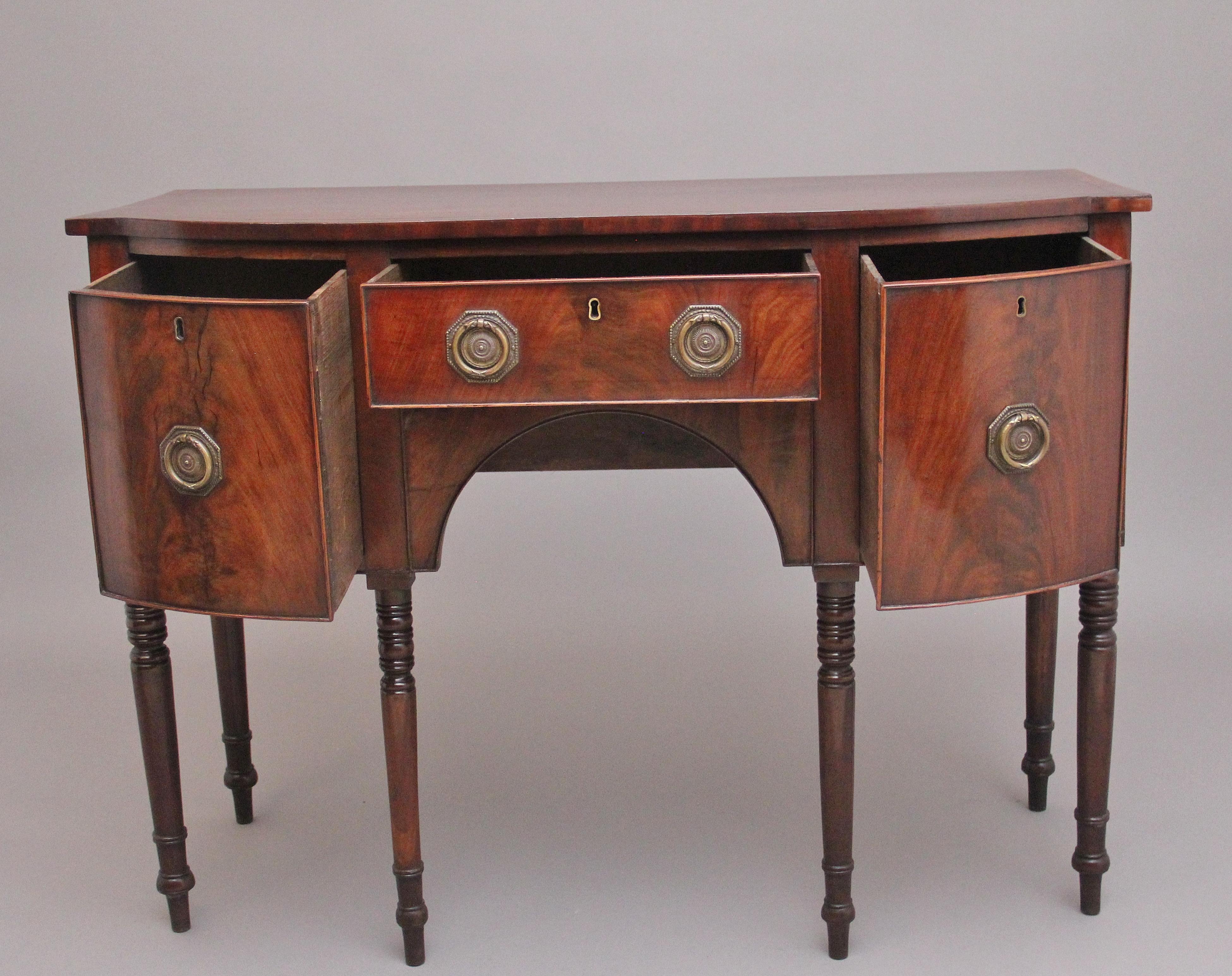 Credenza ad arco in mogano dell'inizio del XIX secolo, il piano sagomato e figurato sovrasta un cassetto centrale affiancato da un cassetto profondo rivestito in Oak con maniglie ad anello e placca in ottone, sostenuto da sei gambe tornite ad