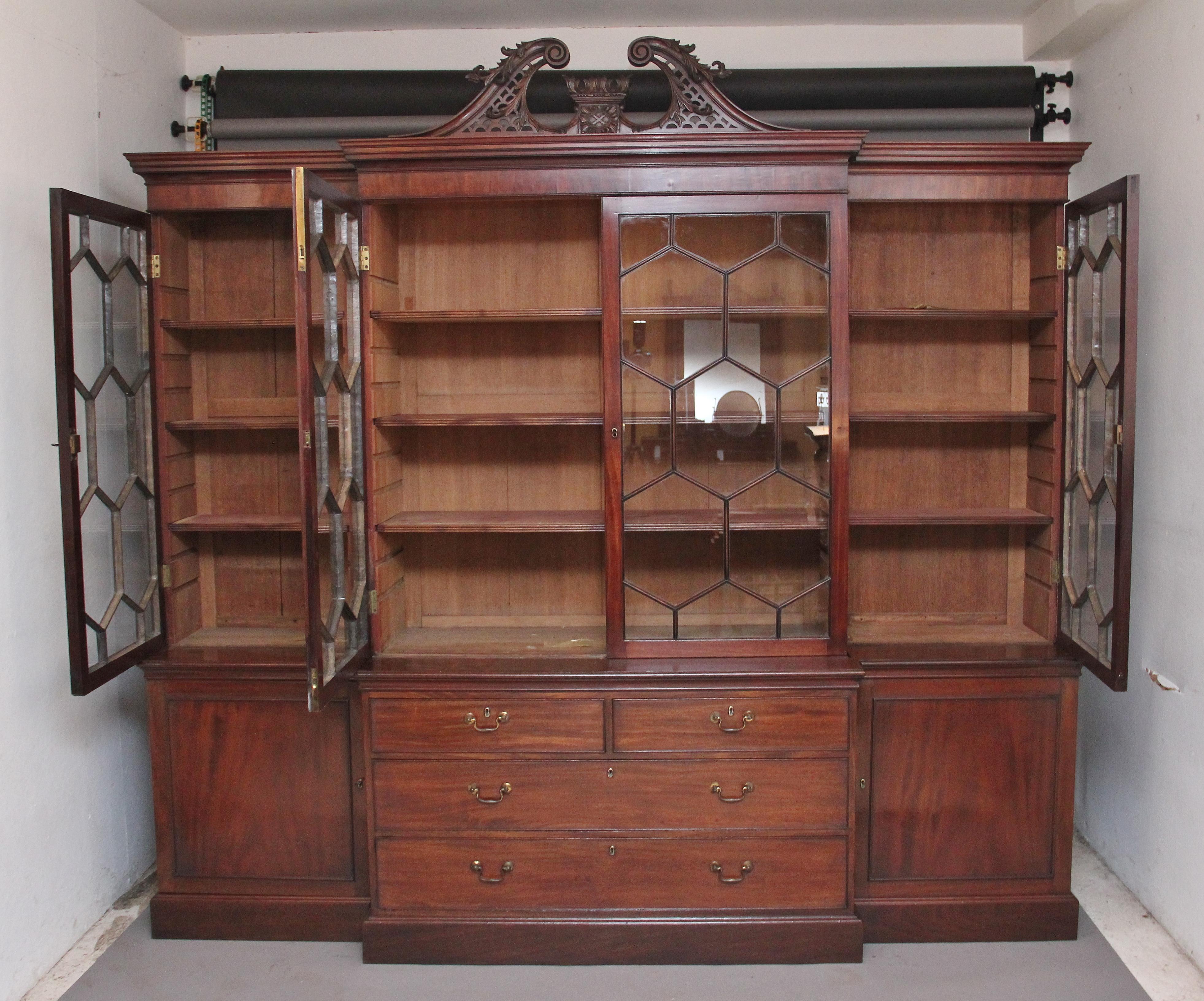 A large early 19th century mahogany breakfront bookcase, with later highly decorative pierced fret swan neck pediment with central carved feature, the stepped moulded cornice above four large astrigal glazed doors opening to reveal three adjustable