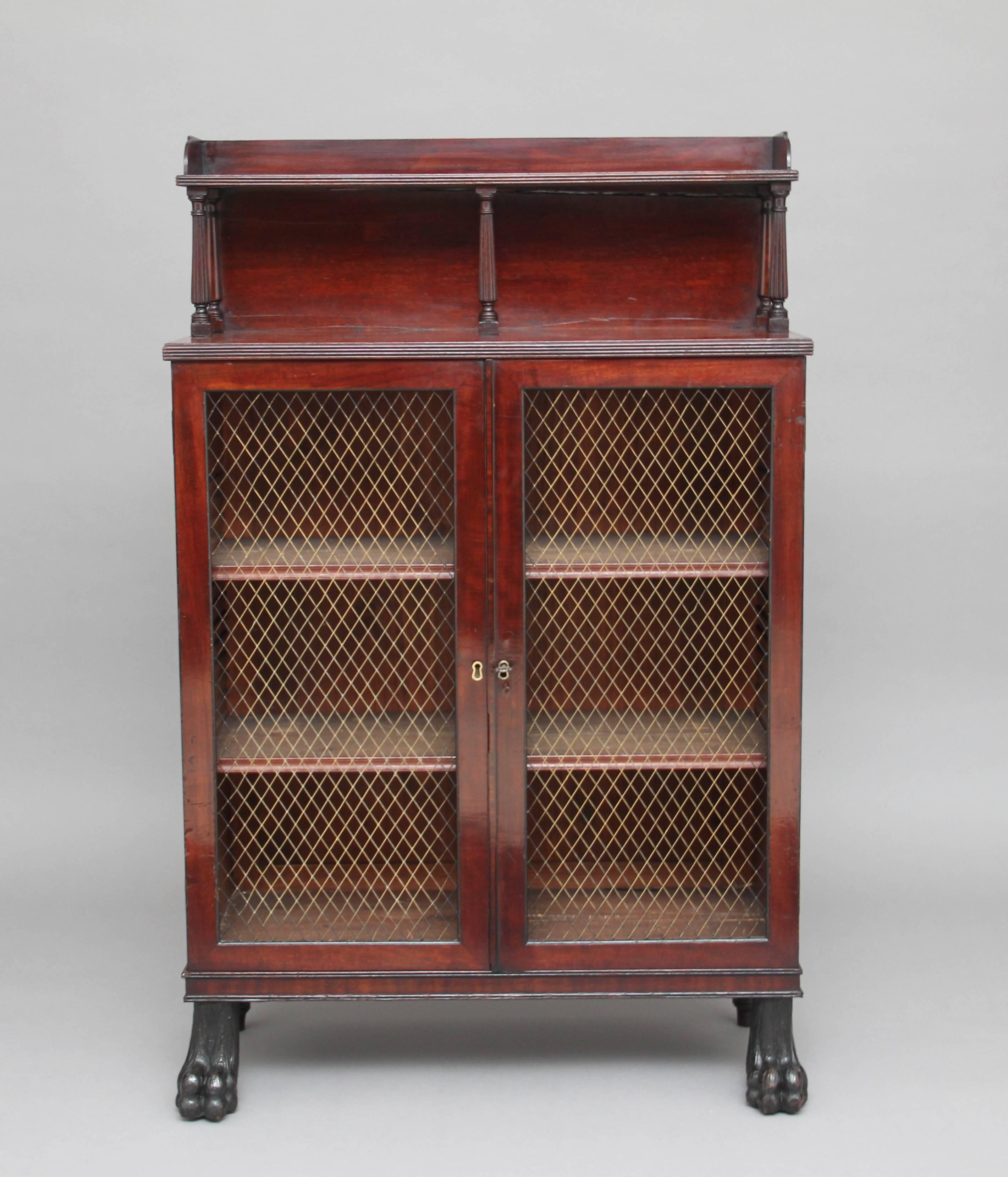 Early 19th century mahogany bookcase or cabinet of good proportions, the top section having a shelf with a reeded edge and a shaped gallery running along the sides and front, supported on five turned columns, the cabinet having two doors with brass