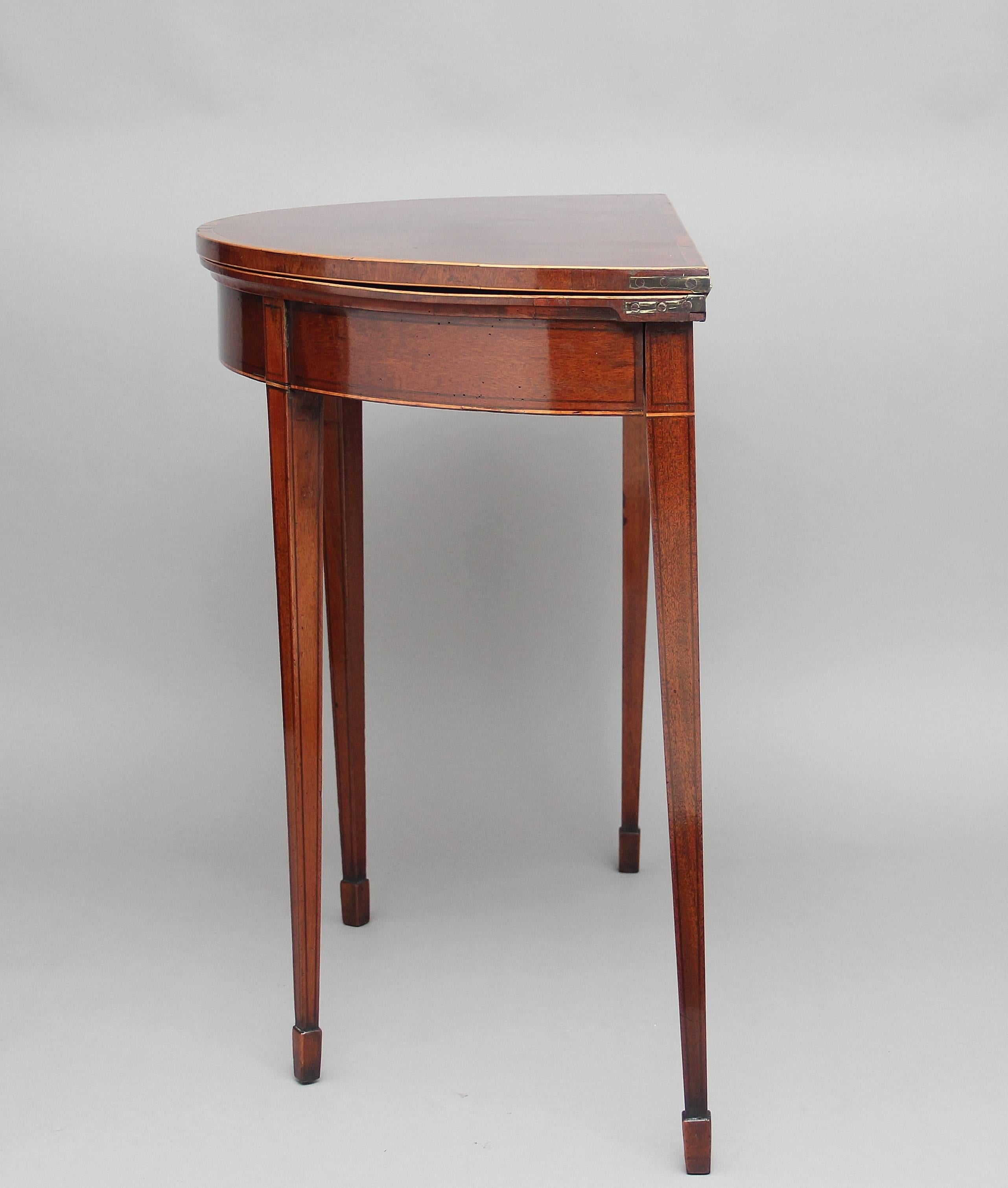 Early 19th century mahogany demilune card table, the semi circular crossbanded top with boxwood stringing opening to reveal a green baize playing surface, supported on square tapered legs terminating with spade feet, circa 1800.