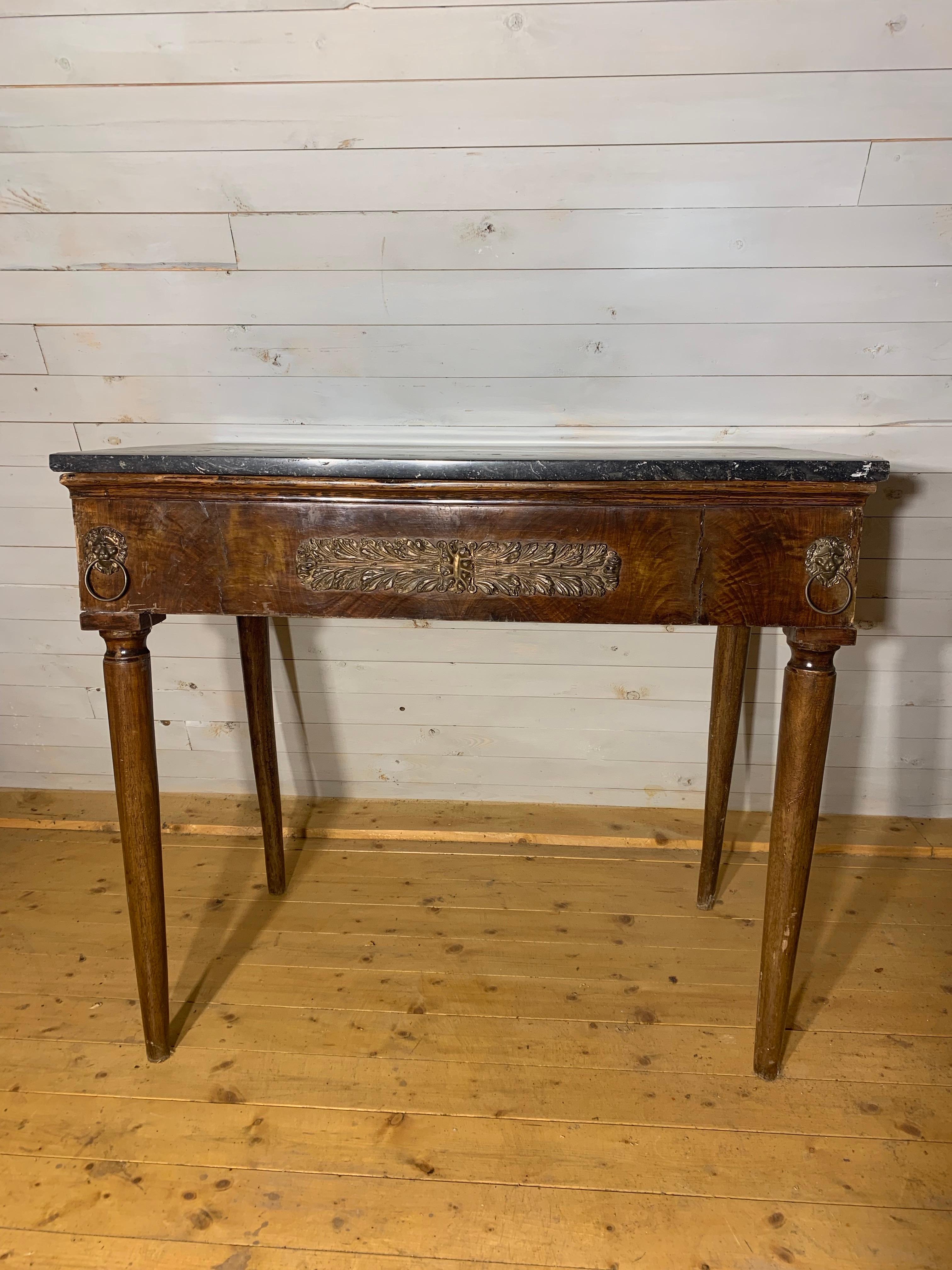 A console table in mahogany and brass decoration in the front. 
The table is made in France during Charles X - period. 
The mahogany has a beautiful aged color with nice patina. On the top there is a black marble stone .

The pair of candlesticks