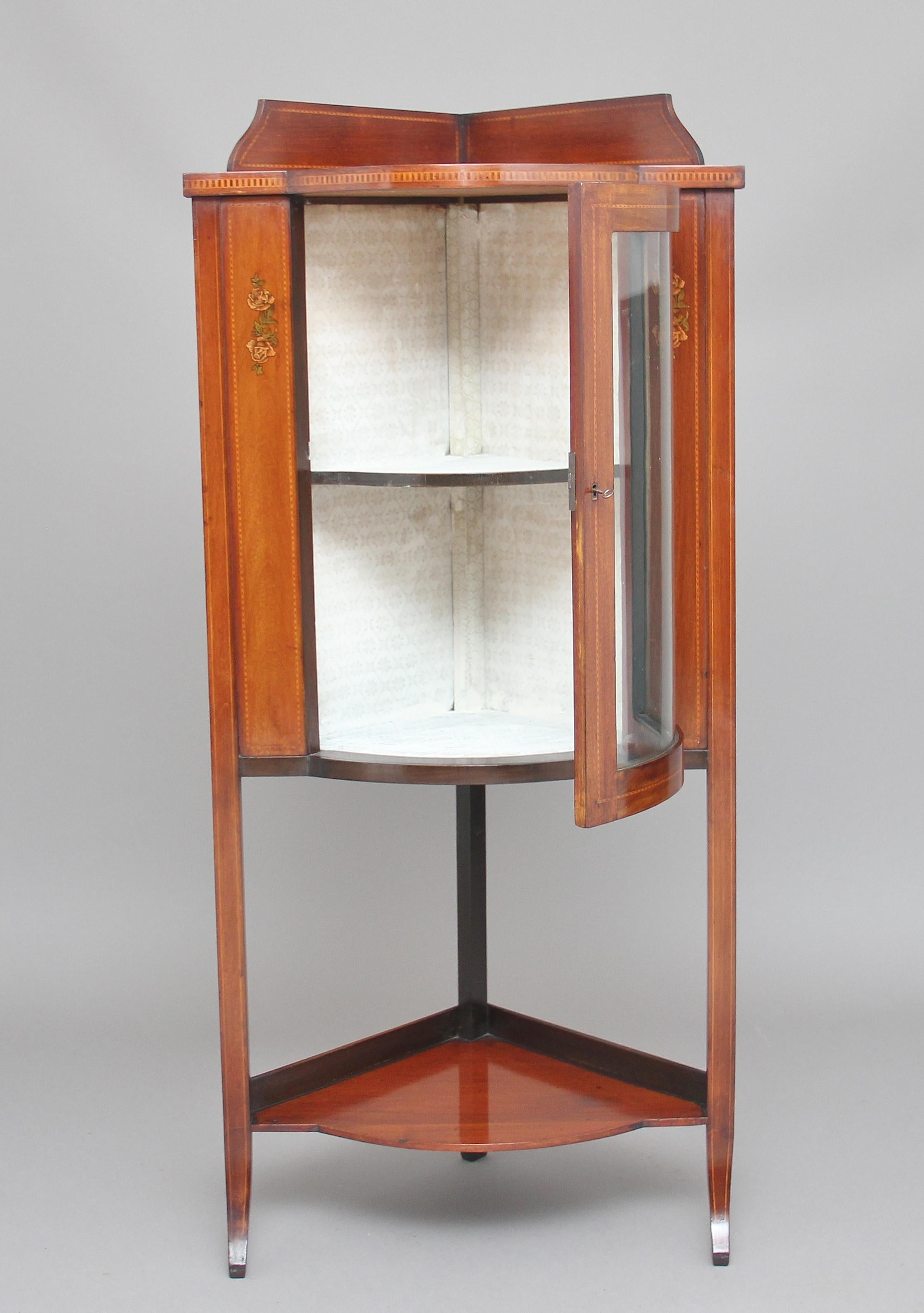 Early 19th century mahogany corner cupboard with a glazed bowfront door with a galleried shelf below and a gallery at the top, inlaid all-over with black and while line and painted floral decoration either side of the door, circa 1910.