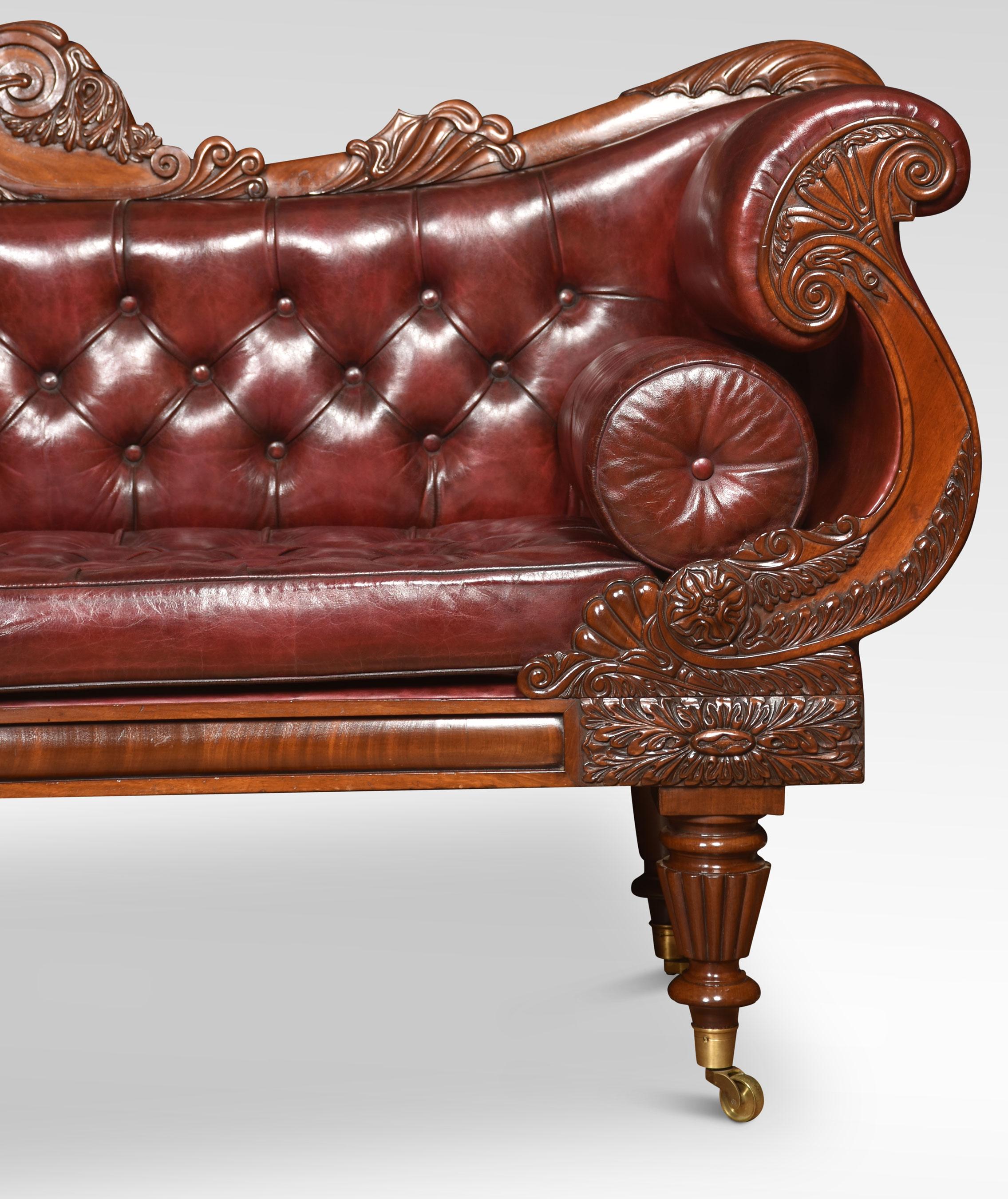 Early 19th-century mahogany framed scroll end settee, the acanthus scrolling arched top rail above deep buttoned back and seat flanked by scrolling burgundy leather arms. Standing on foliated carved tapered reeded legs with brass caps and