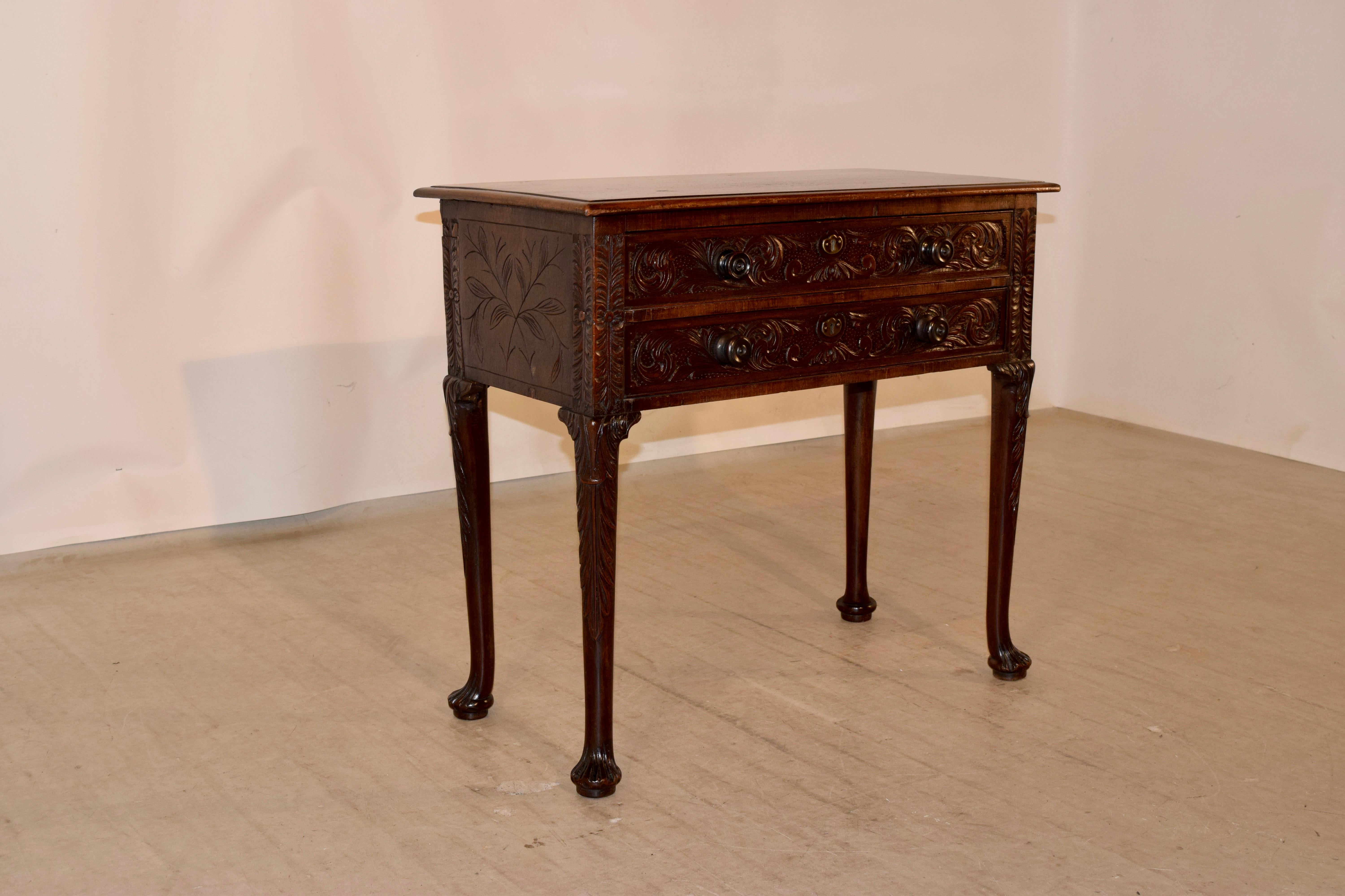 Early 19th century mahogany side table from England with a wonderfully grained top with beveled edges, following down to hand carved sides and two drawers in the front. The entire case is expertly hand carved decorated, and the table is supported on