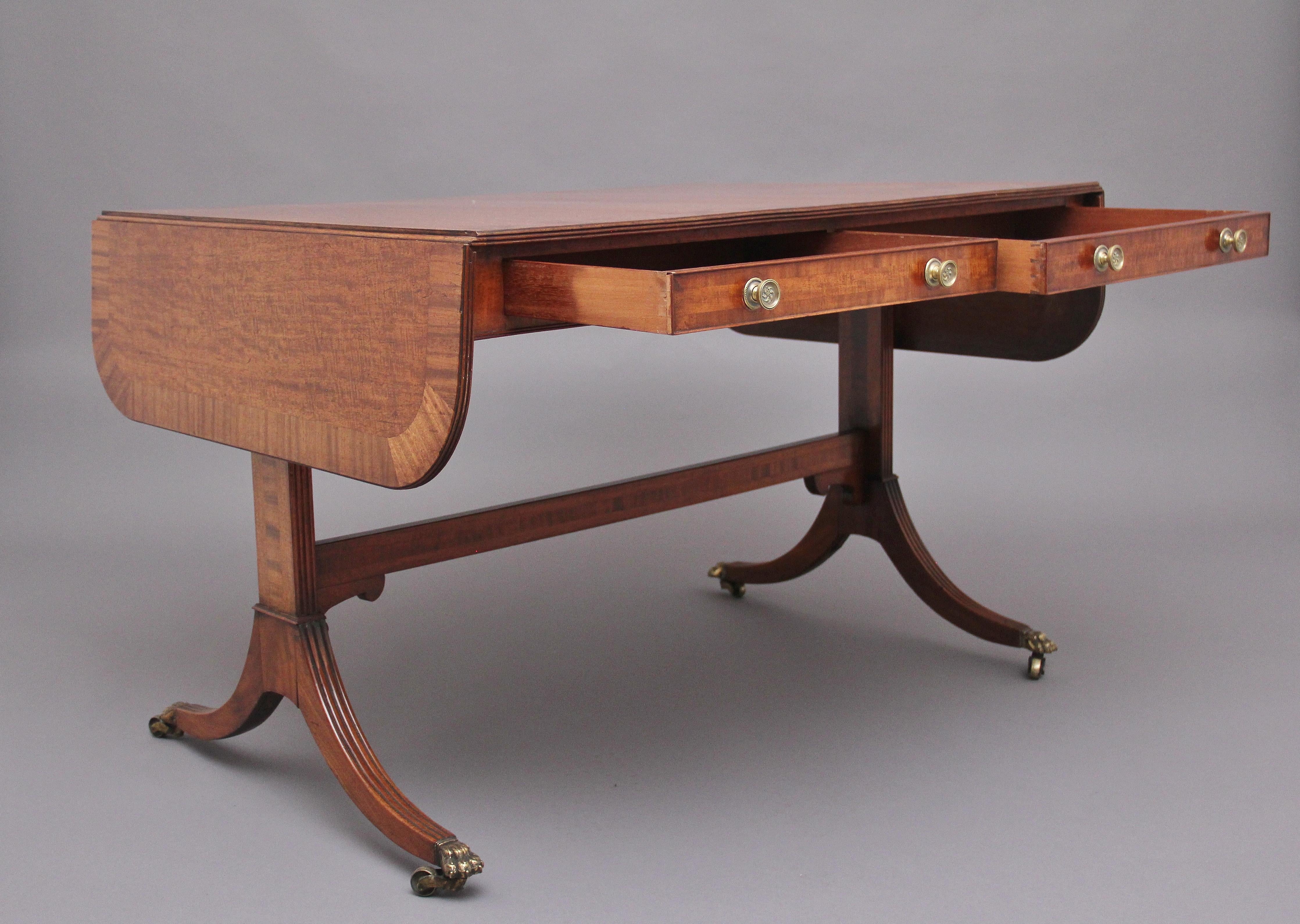Early 19th century mahogany sofa table, having a lovely figured top which is crossbanded and having a reeded edge, having two drawers either side with engraved brass knob handles, the end supports united by an inlaid stretcher, standing on reeded