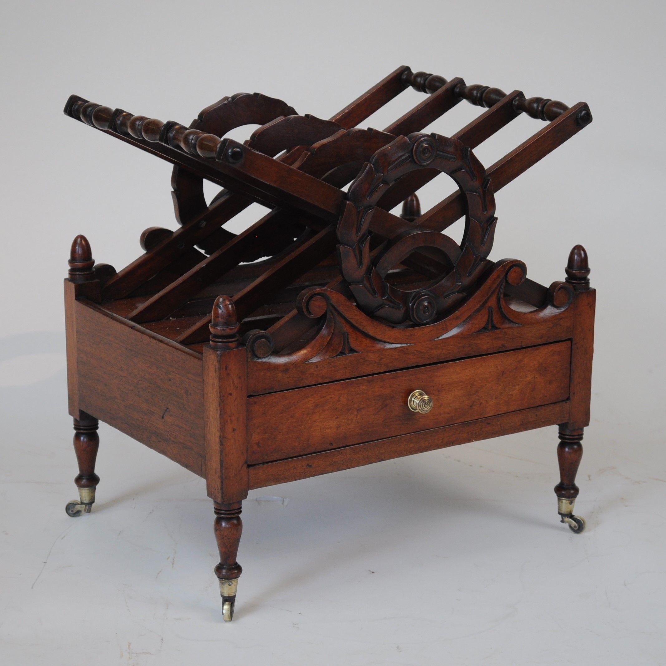 A good quality early 19th century mahogany Canterbury carved with a laurel wreath to the front and with 'X' shaped dividers, standing on slender turned legs with original brass castors, and with original turned wooden handles to the drawer.