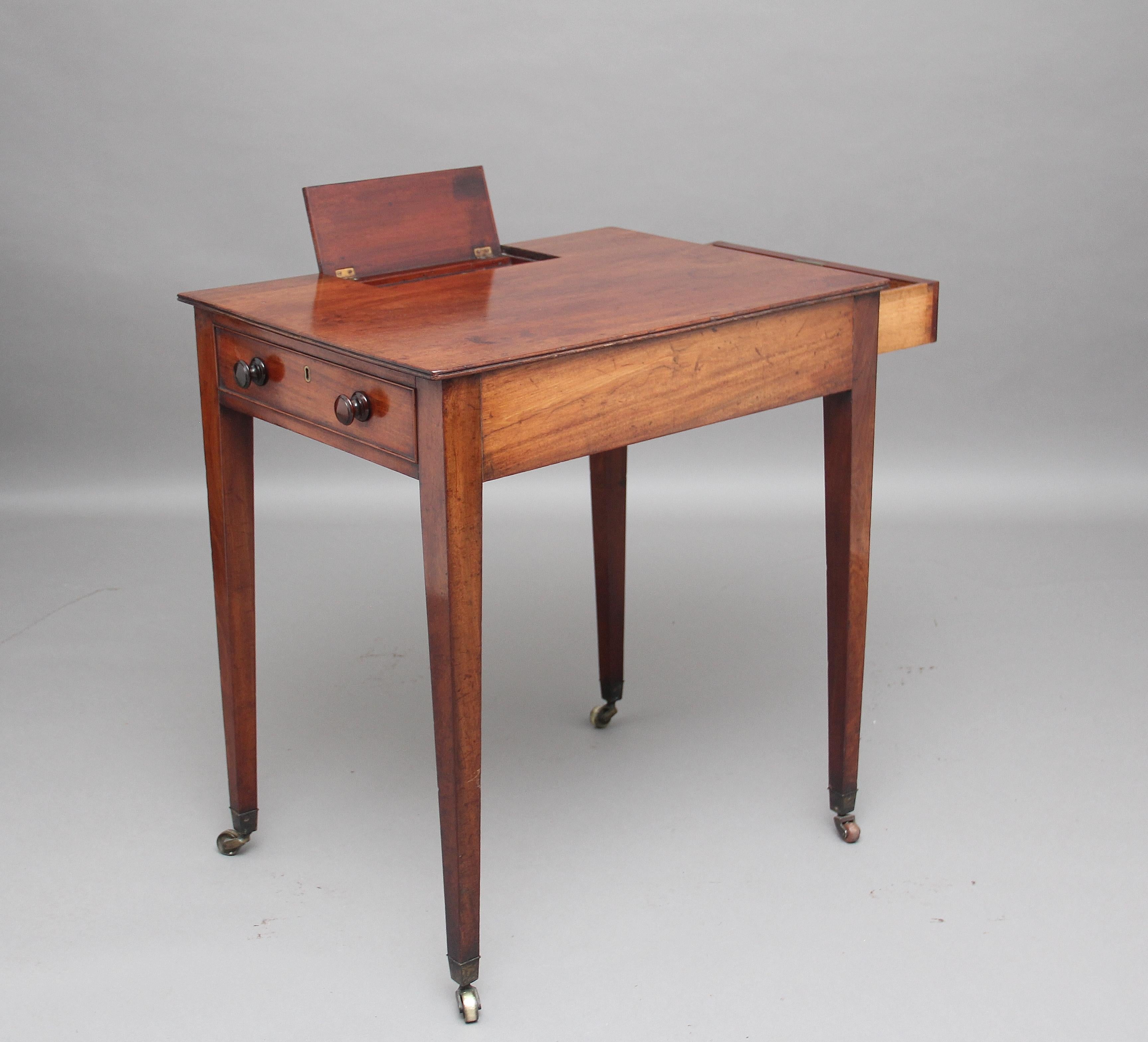 Early 19th century mahogany writing or side table on square tapered legs and castors, with a drawer on one end and a faux drawer on the other end, the top has a lift up flap to reveal a pen tray, two compartments for ink wells and another central