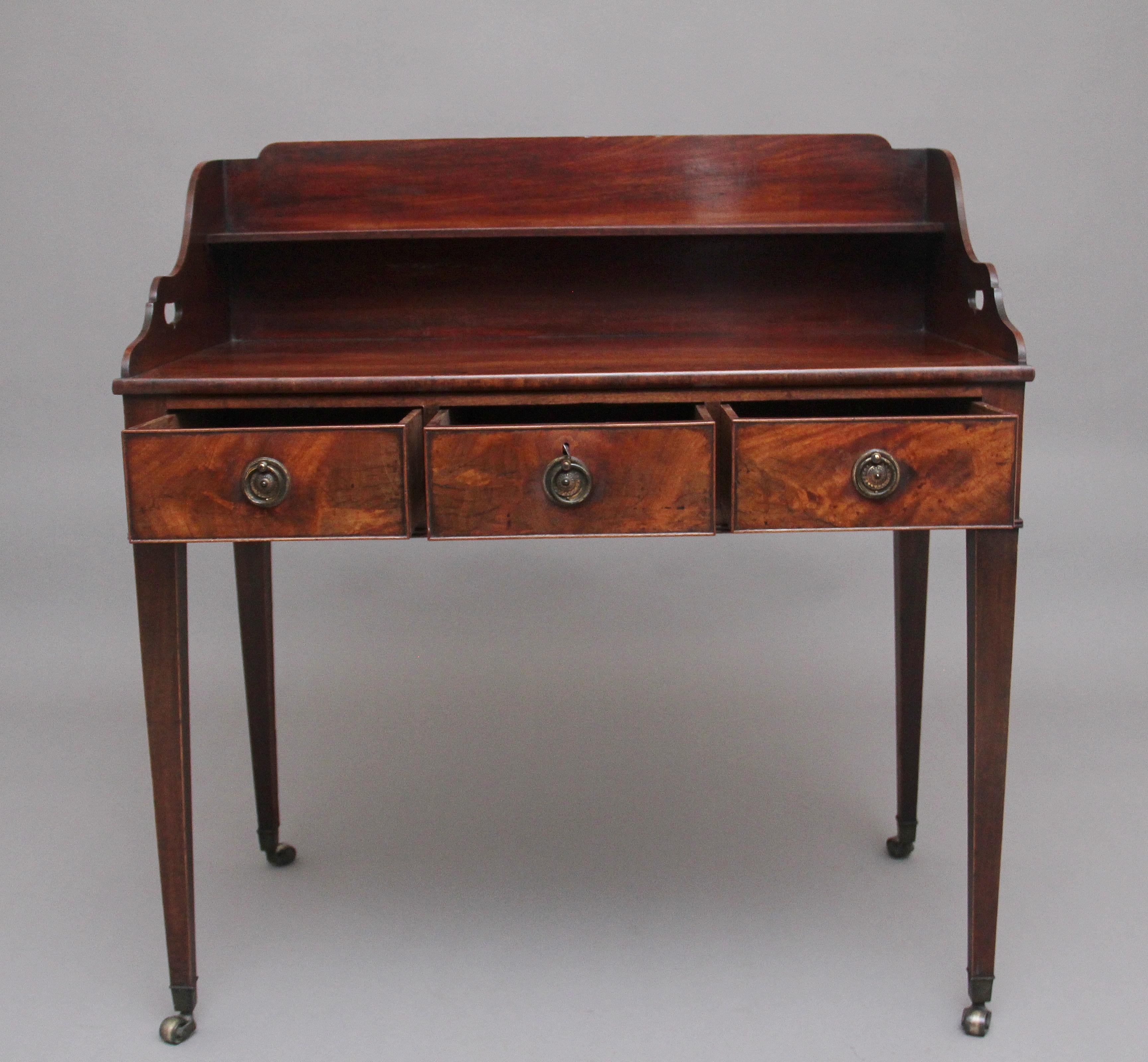 A lovely quality early 19th century mahogany writing table, having a shaped gallery with a shelf, fret cut out carrying handles at the sides of the gallery, three frieze drawers with the original brass ring handles, lovely figuration on the drawer