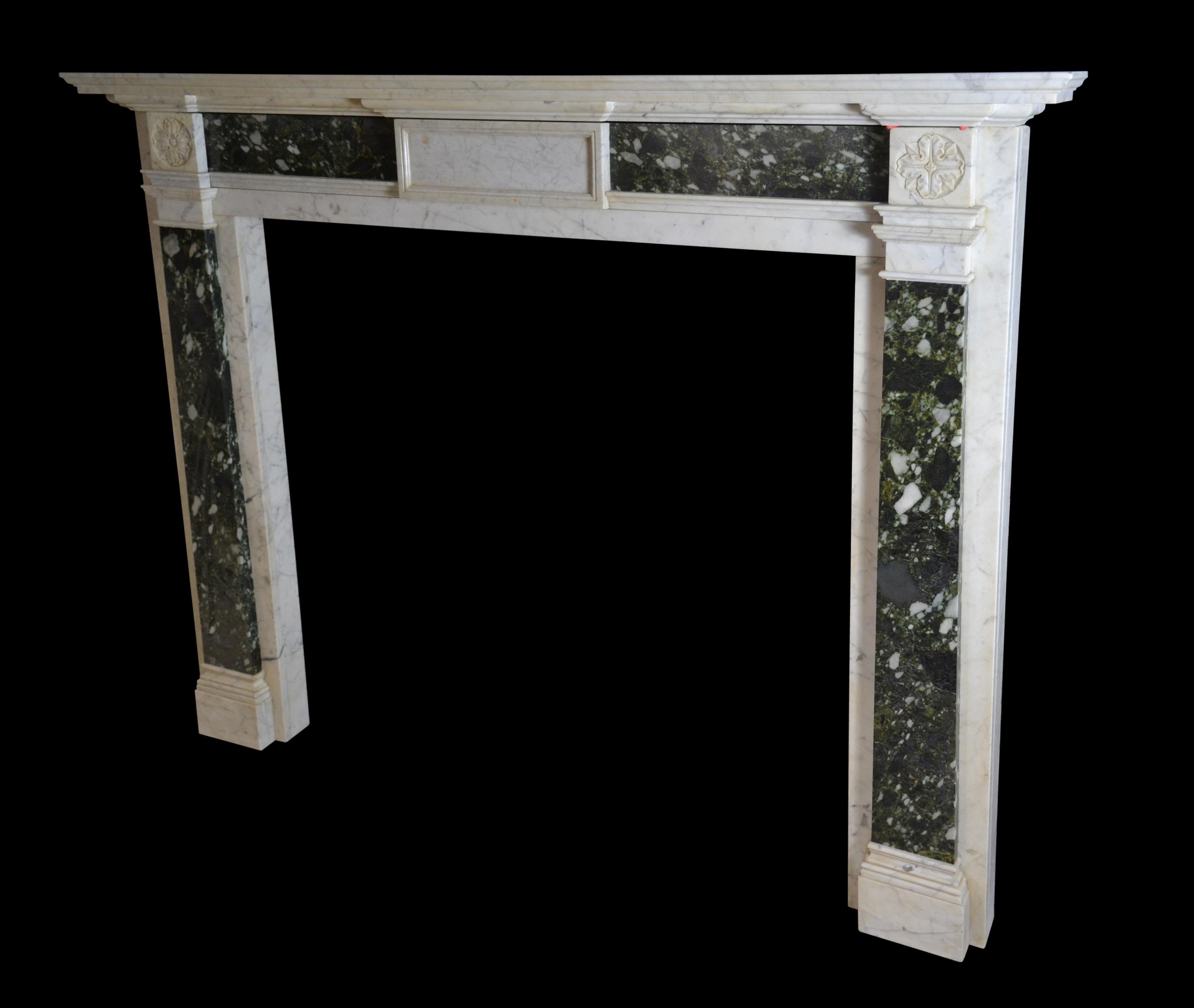 An early 19th century mantelpiece of architectural form in Carrara marble with end blocks carved with simple rosettes above inverted tapering pilasters in brecciated verde marble and conforming frieze panels, the latter flanking a plain fielded