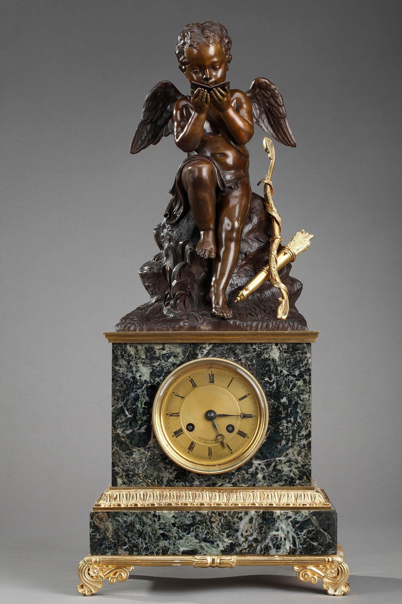 Pendule en marbre vert-de-mer du début du XIXe siècle, d'époque Restauration, avec décoration en bronze doré. L'horloge est surmontée d'un Cupidon en bronze patiné. Le cadran en bronze doré indique les heures en chiffres romains et est décoré de